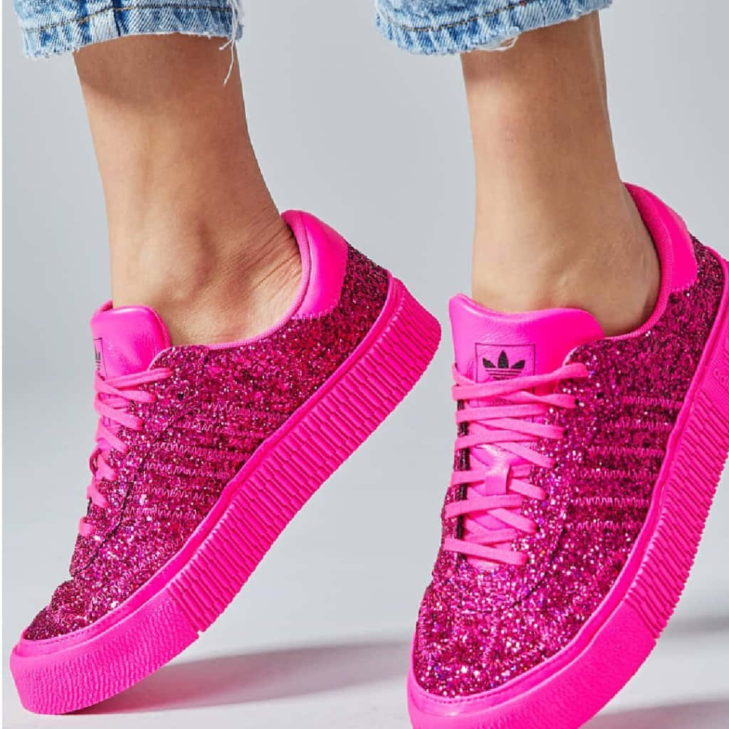 Pink Shoes 桌布 壁紙 — 鮮豔的粉紅色閃粉運動鞋，搭配厚底，與捲起的牛仔褲一起穿著，背景為純色。