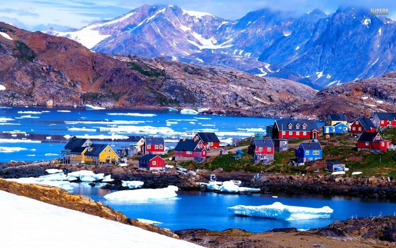 Greenland 桌布 壁紙 — 鮮豔的紅色、黃色和藍色房屋緊貼著白雪覆蓋的海岸，旁邊是冰冷的海水和高聳的雪山。