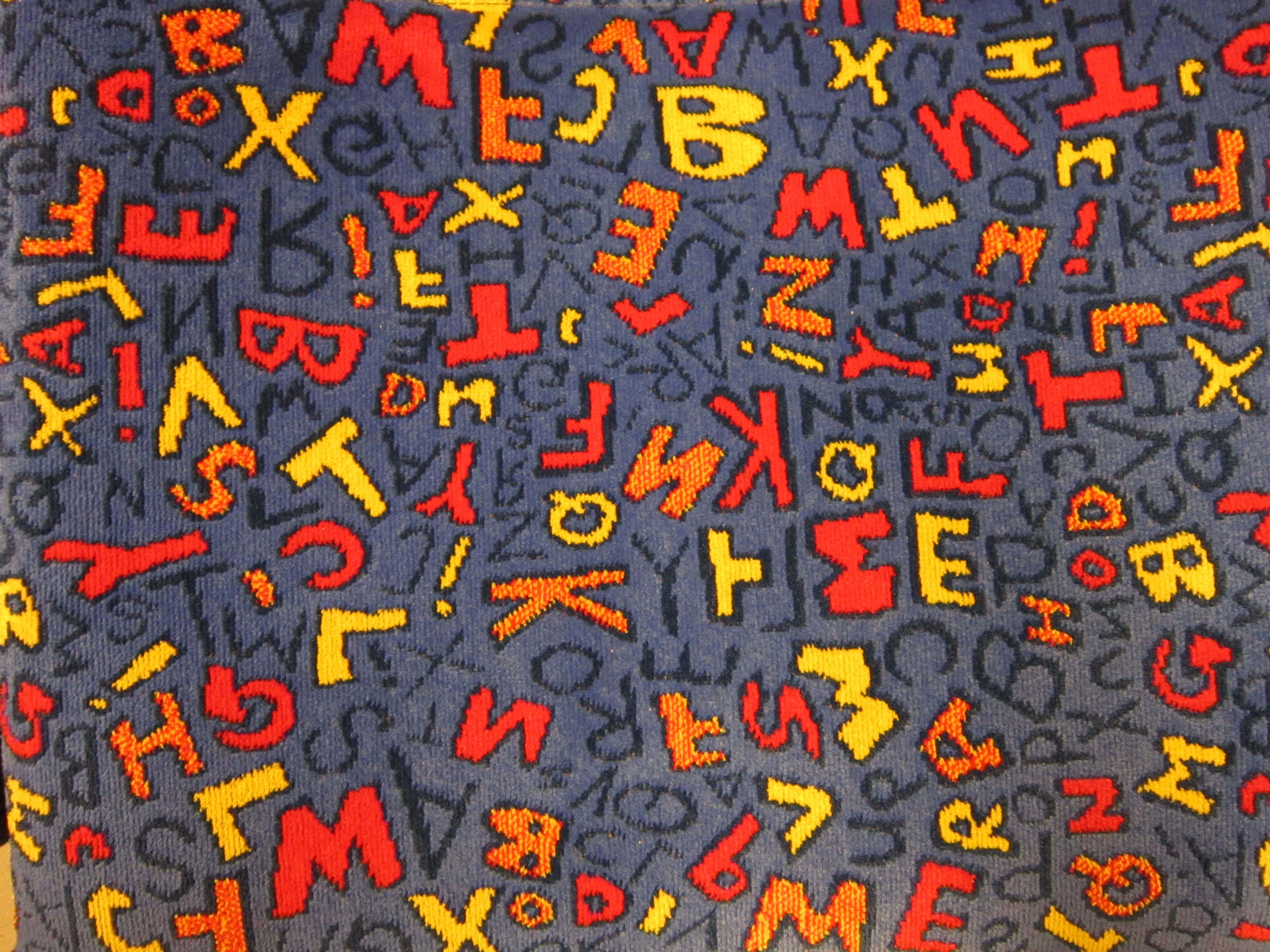 字母 桌布 壁紙 — 鮮豔的紅色和黃色字母雜亂地散落在有紋理的深藍色布料表面上。