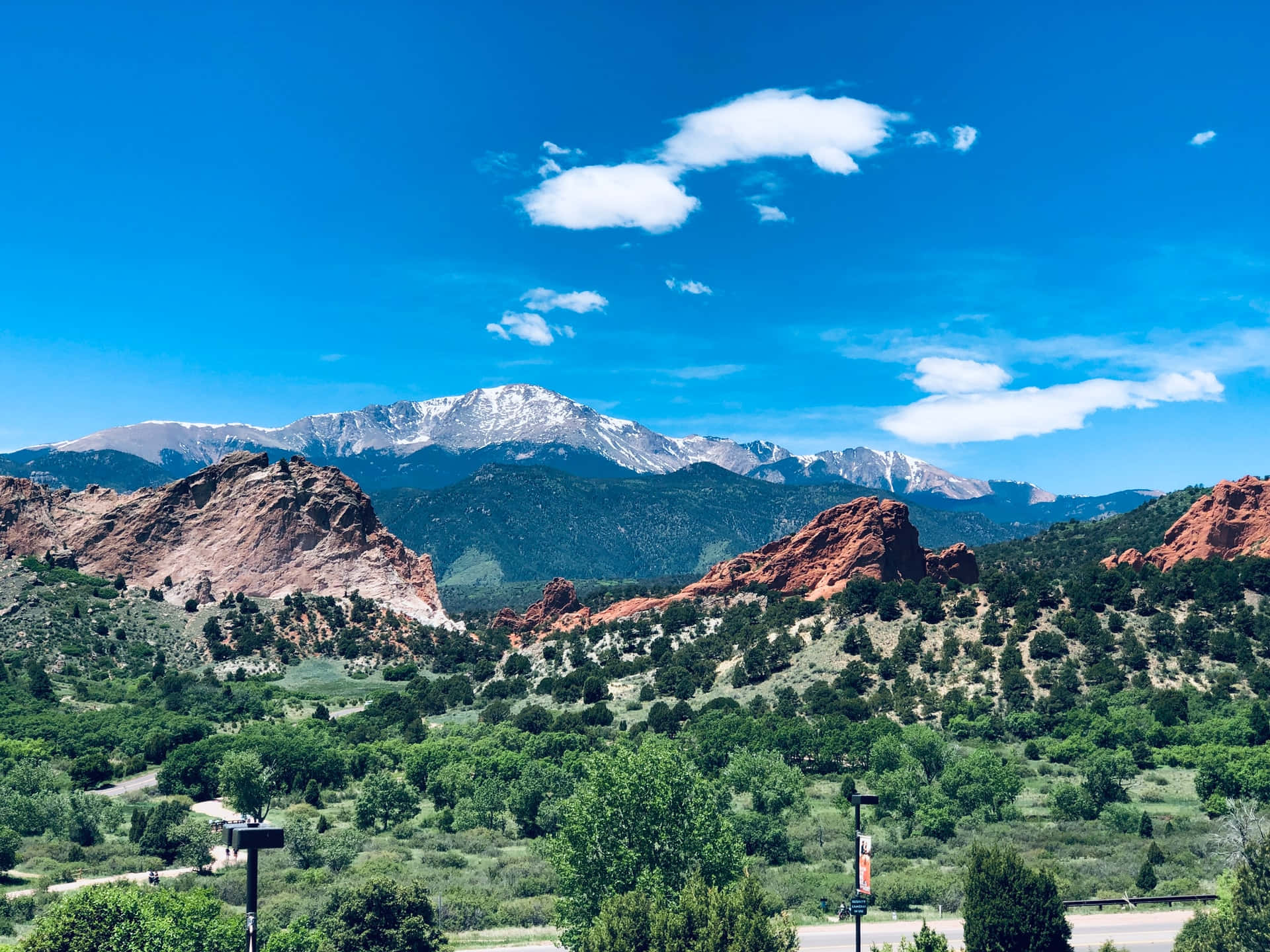 Colorado 桌布 壁紙 — 鮮豔的紅色岩層從鬱鬱蔥蔥的綠色山谷中升起，在湛藍的天空下，點綴著散落的白色雲朵。