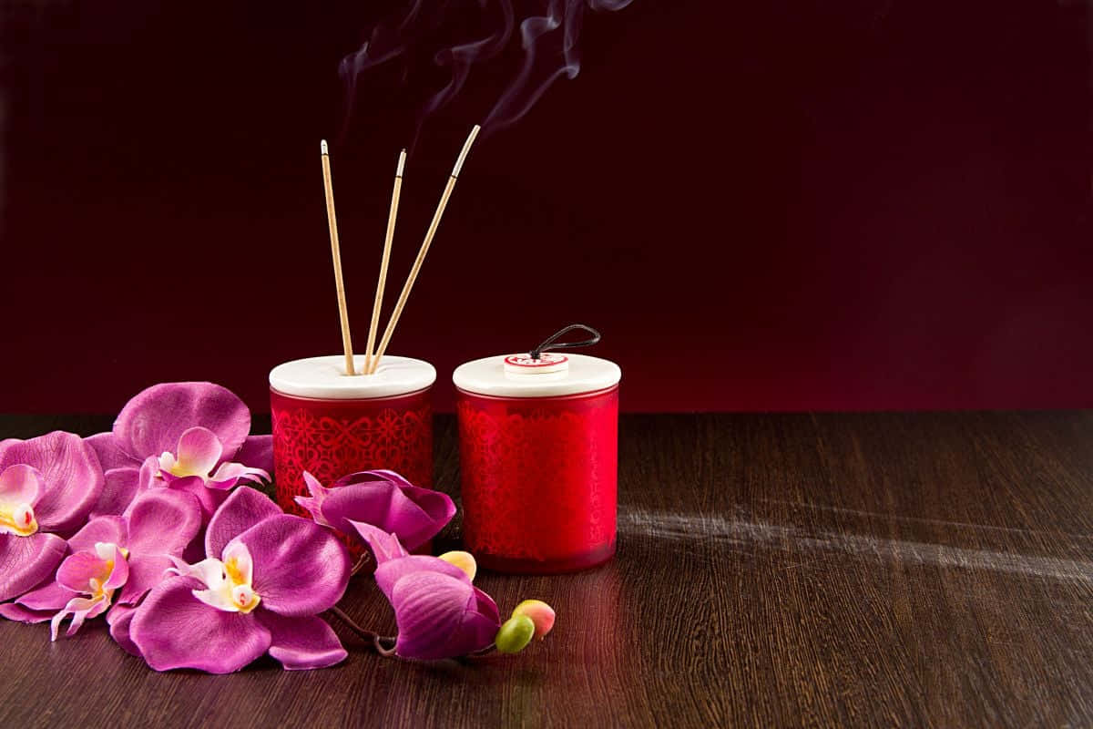 Aromatherapy 桌布 壁紙 — 鮮豔的紫色蘭花和紅色香爐，煙霧裊裊，放置在深紅色背景前的深色木質表面上。
