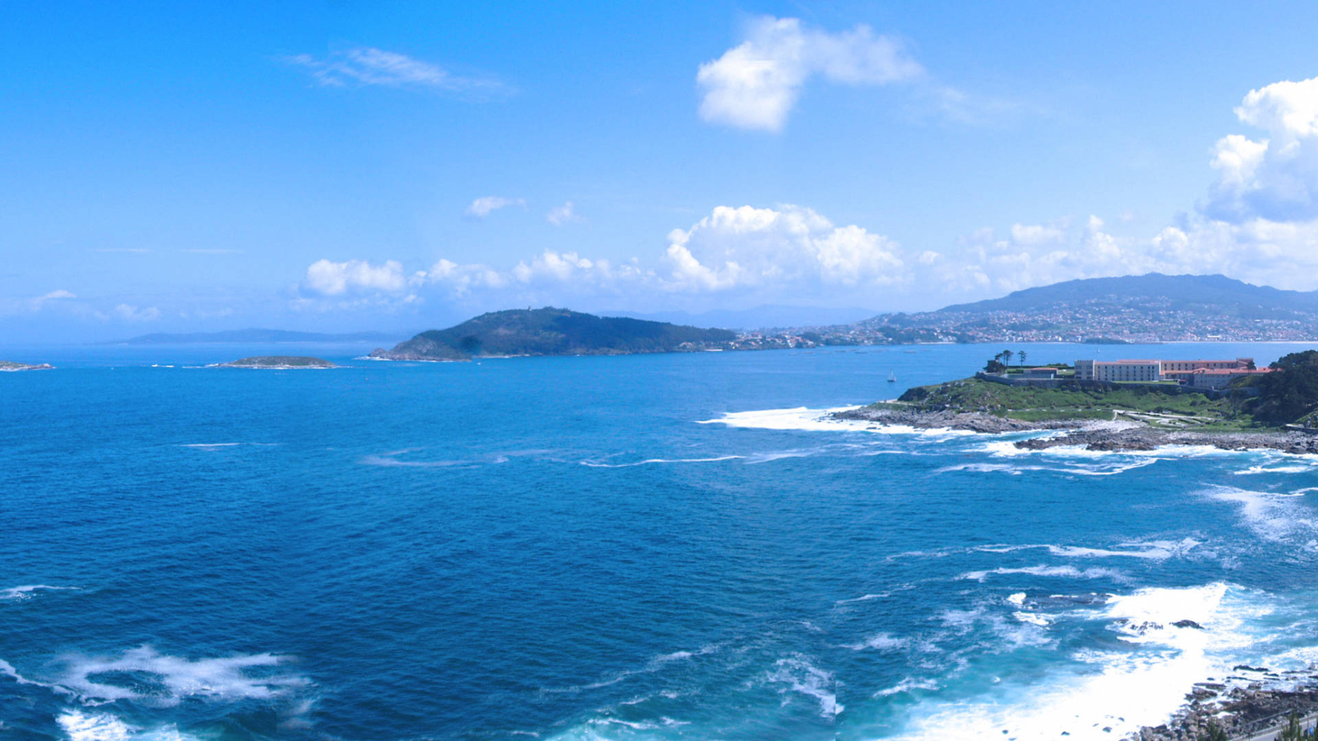 陽光明媚的天空下，海浪拍打和遠山構成的海岸景色。