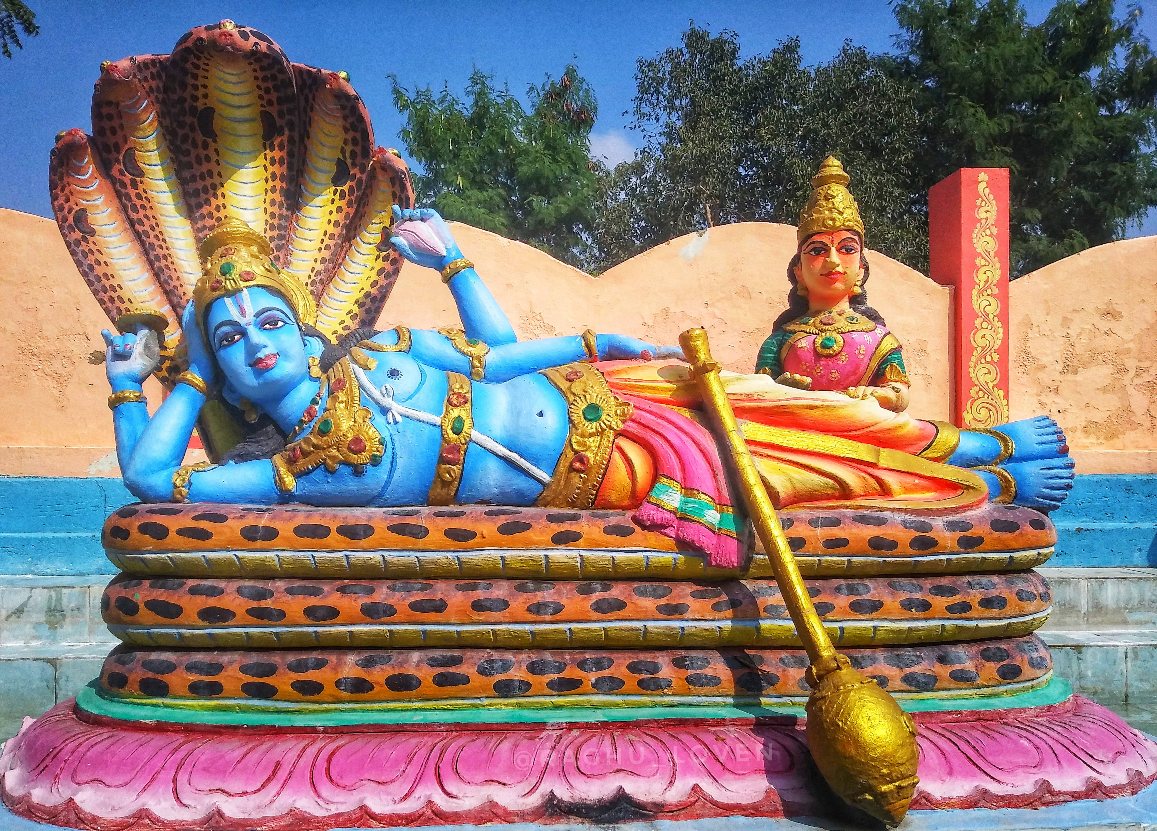 Lakshmi 桌布 壁紙 — 鮮豔的藍色濕婆神像倚靠在蛇上，伴侶帕爾瓦蒂在他身邊，在晴朗的藍天下。