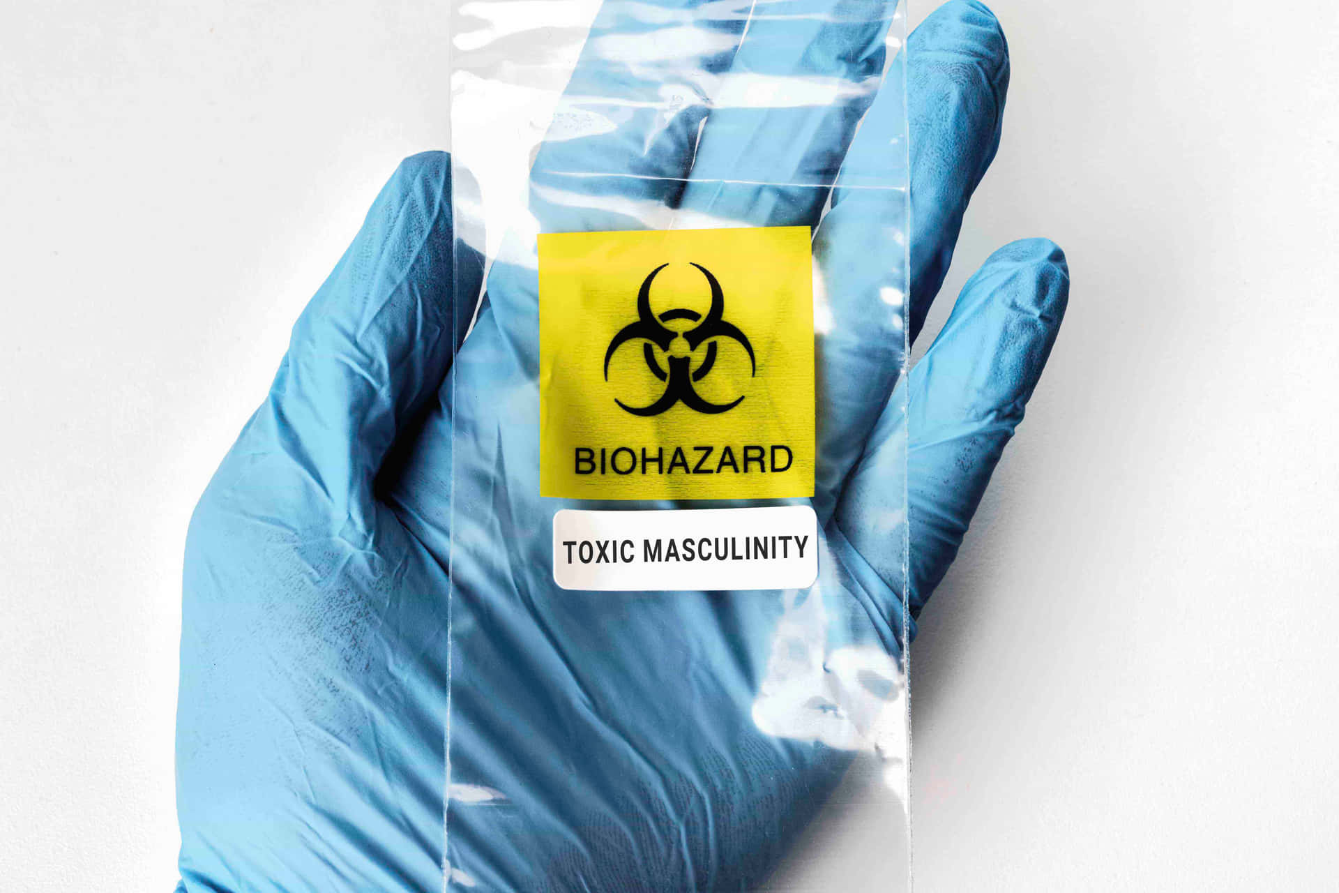 藍色手套的手拿著標有 toxic masculinity 的生物危害袋。