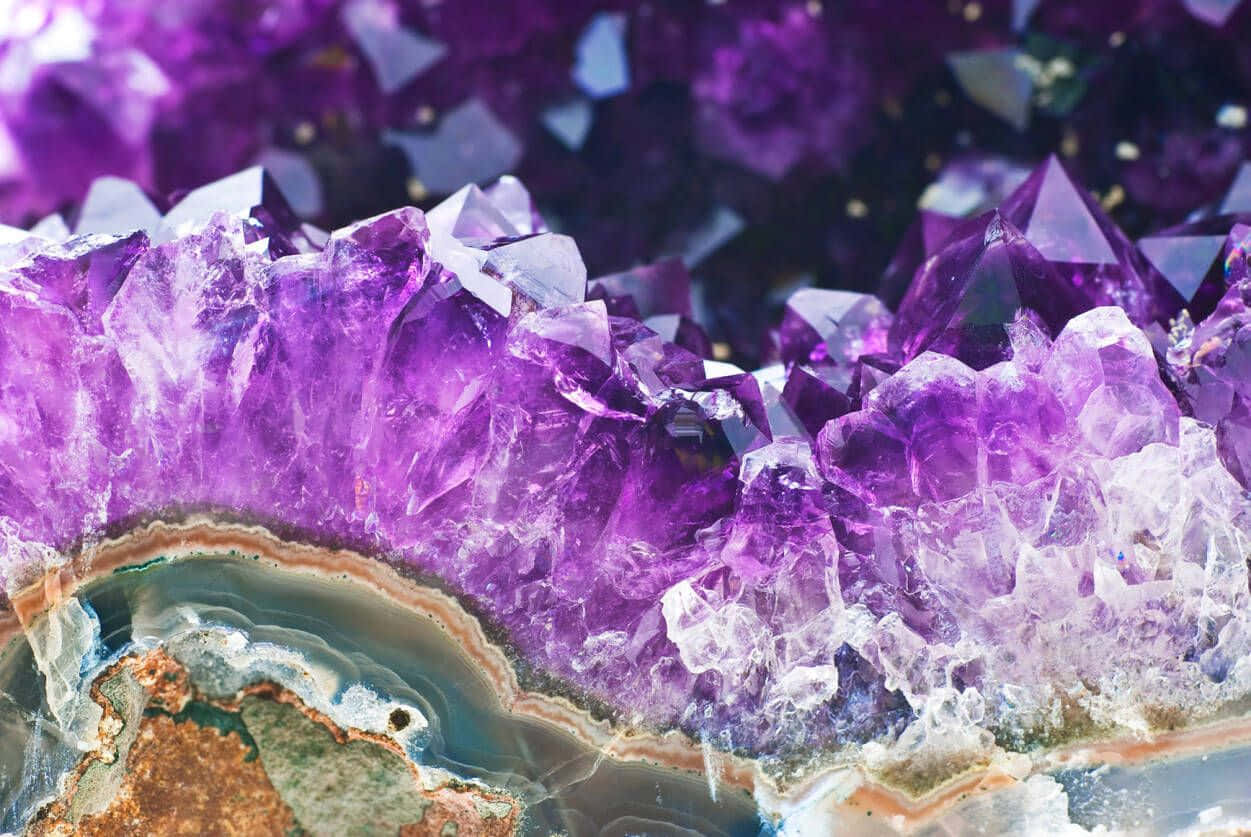 Amethyst 桌布 壁紙 — 鮮豔紫色紫水晶晶體密集簇生，帶有銳利刻面及半透明光澤，生長於層狀瑪瑙基底上。