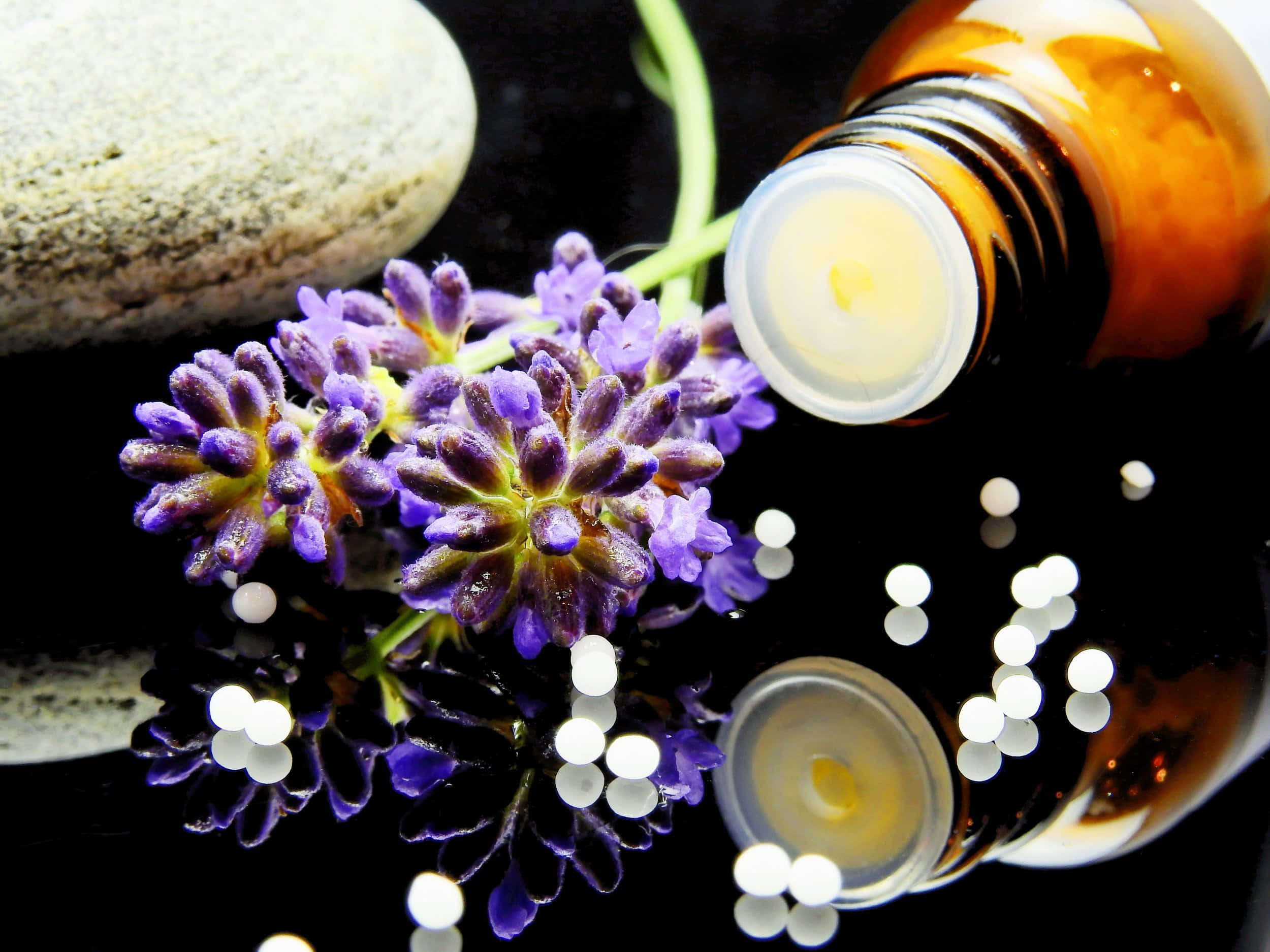 Aromatherapy 桌布 壁紙 — 鮮豔紫色薰衣草花朵的特寫，旁邊是一個裝有琥珀色液體的玻璃瓶和白色藥丸，放在光滑的黑色表面上。