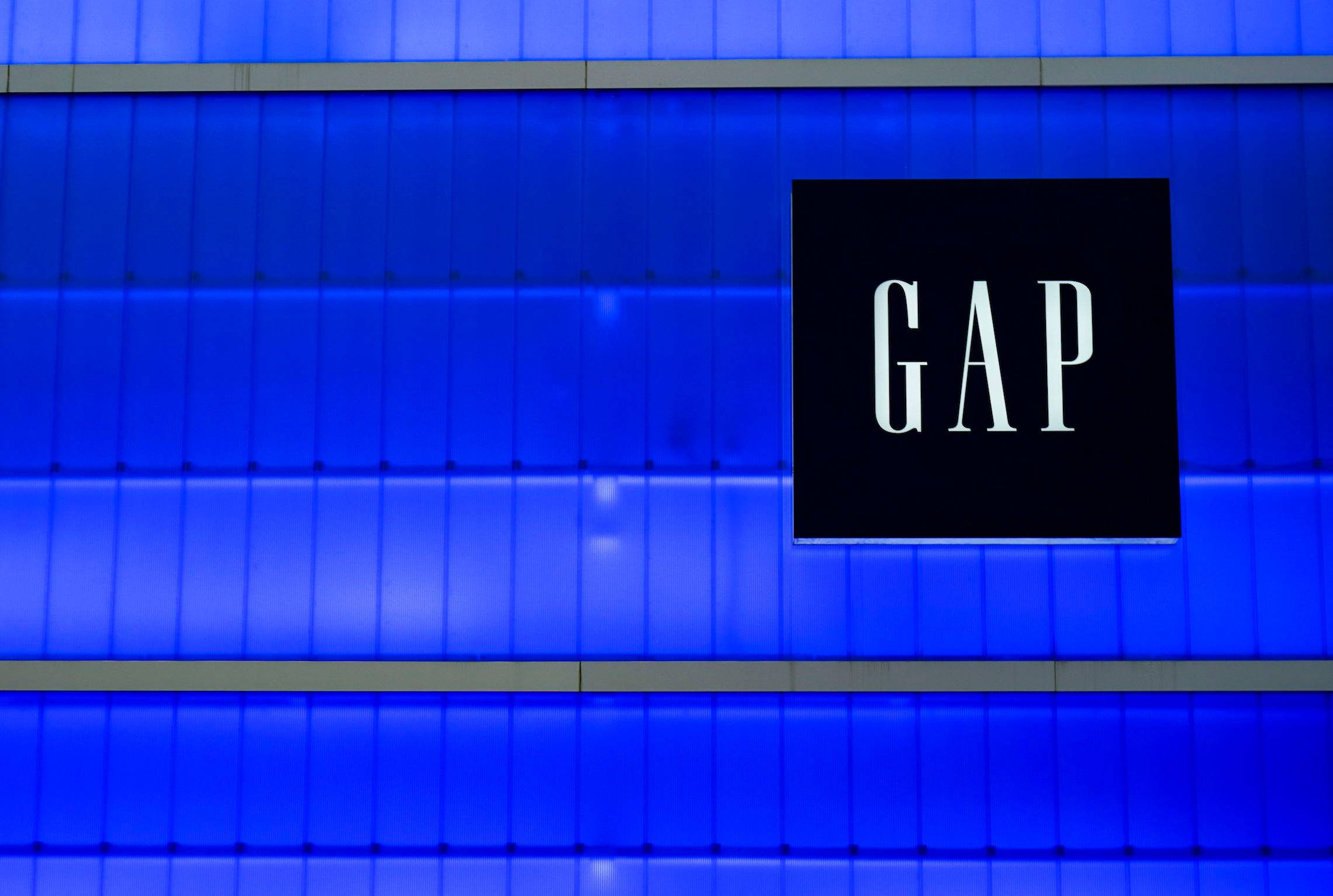 鮮豔藍色Gap標誌 壁紙 — 夜晚，GAP 商店標誌在充滿活力的藍色鑲板建築外牆上發出白色光芒。