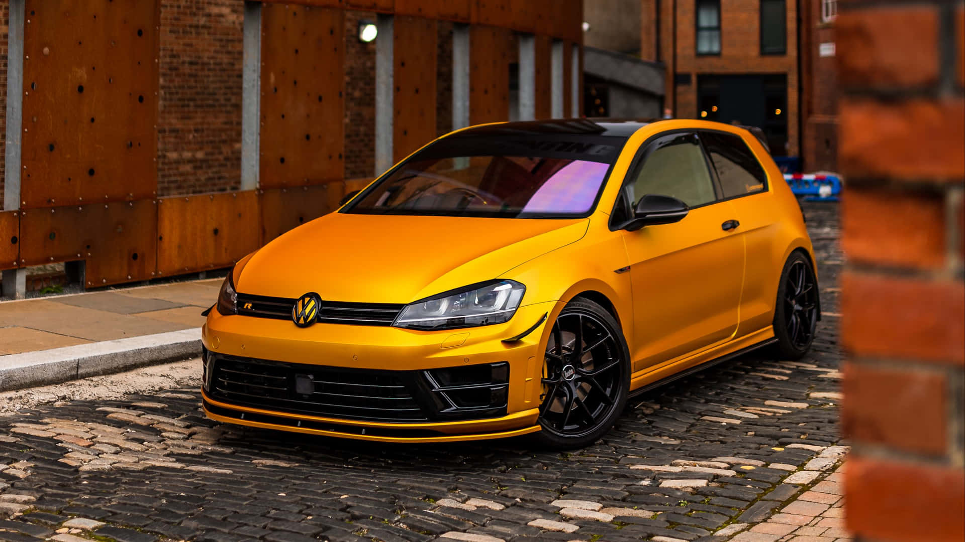 夜晚停在鵝卵石街道上的黃色Volkswagen Golf R。