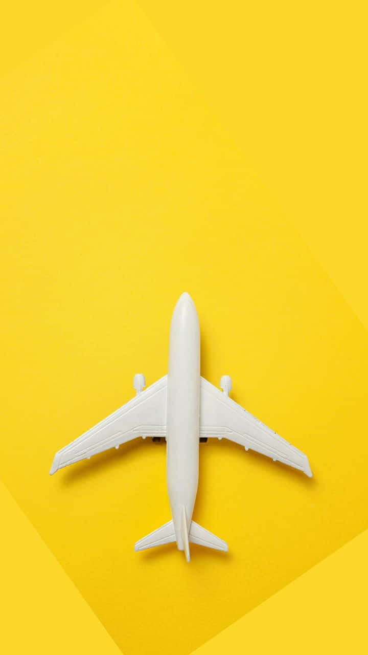 鮮黃色 720p 旅行背景：飛機 壁紙 — 一架白色玩具飛機居中放置在充滿活力的黃色背景上，帶有柔和的對角線陰影。