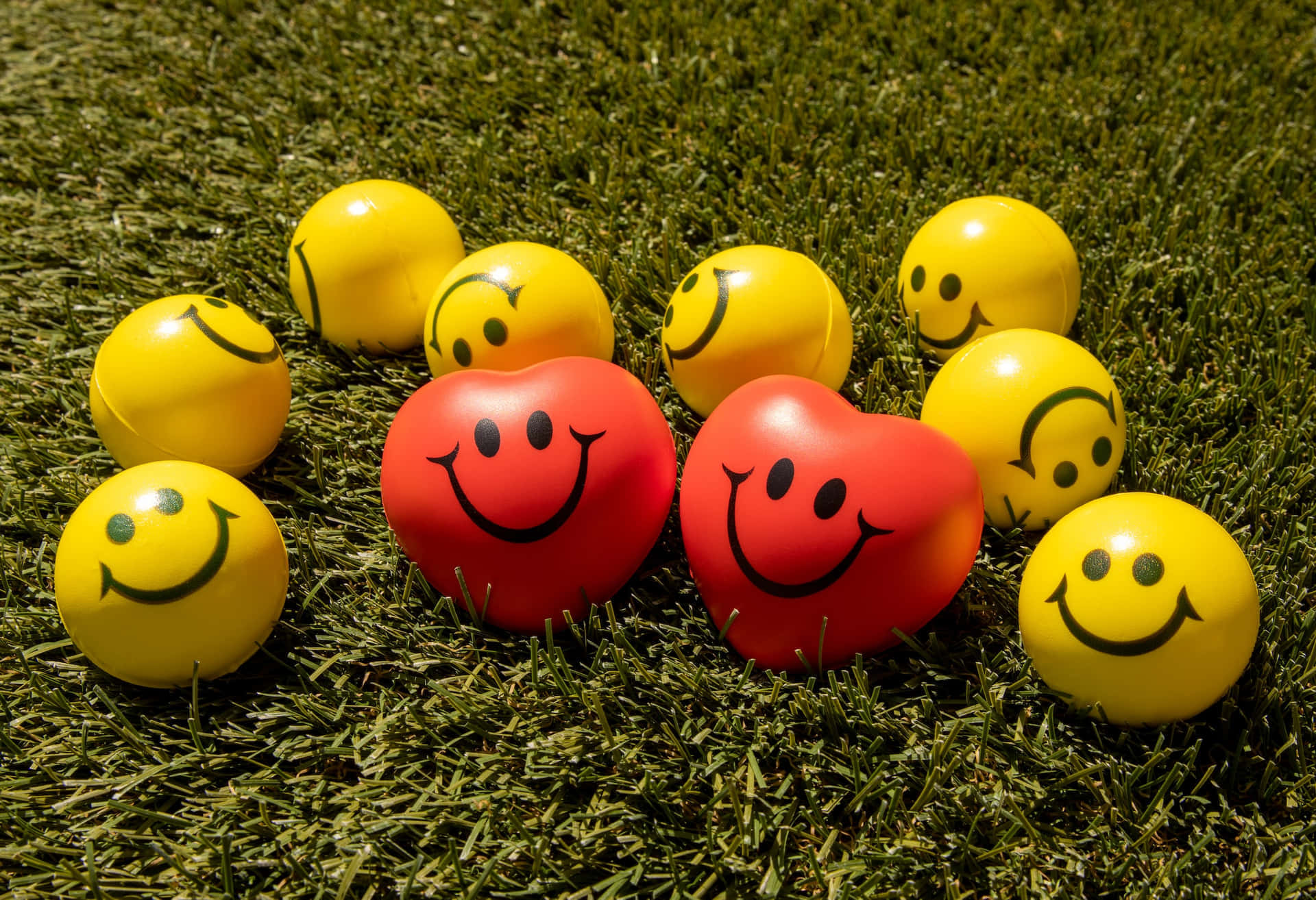 Smiley 桌布 壁紙 — 鮮黃色和紅色的笑臉波波在陽光下放在充滿活力的綠色草地上。