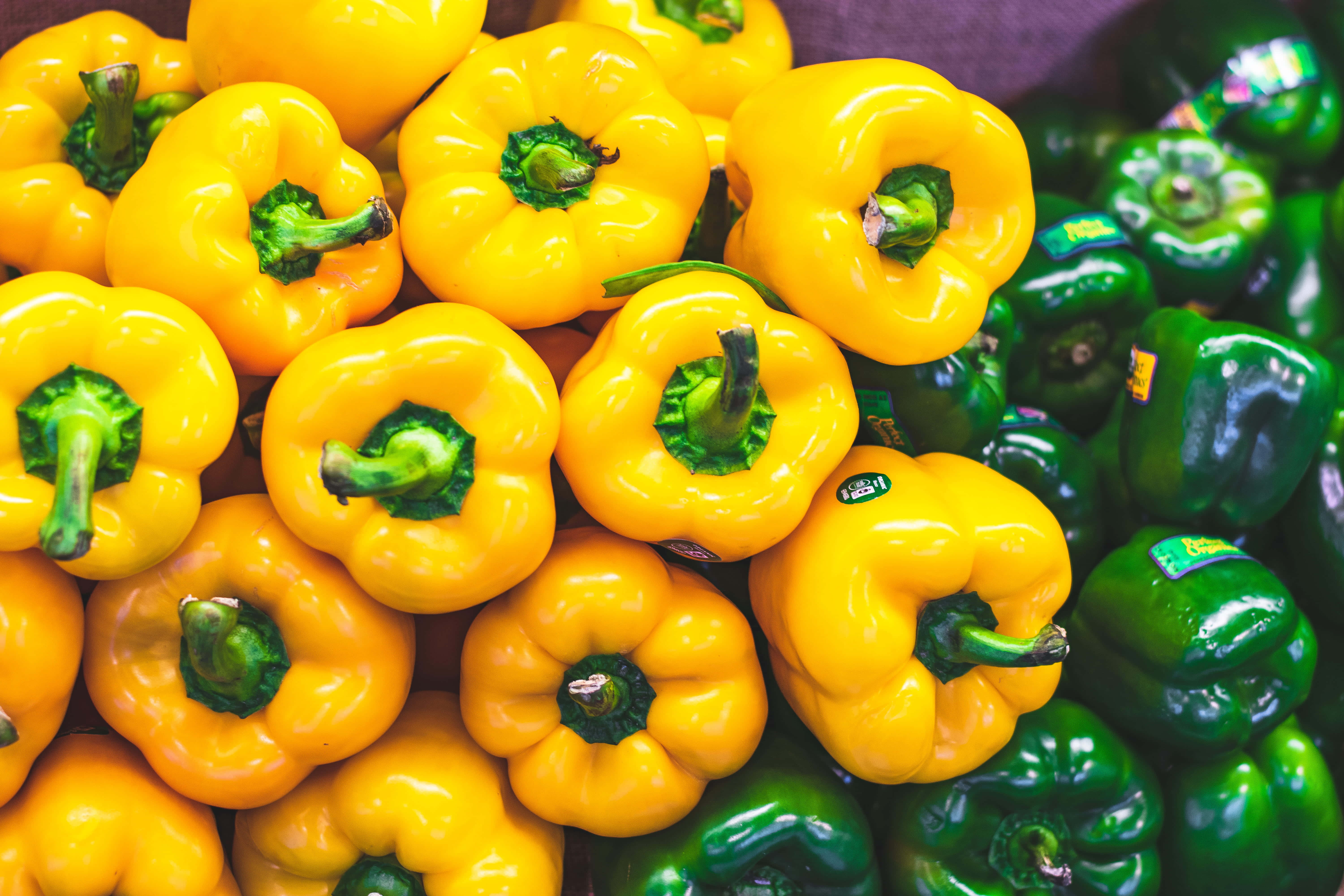 Yellow Bell Pepper 桌布 壁紙 — 鮮黃色和綠色的燈籠椒高高堆疊，表皮光滑，帶有綠色莖部。