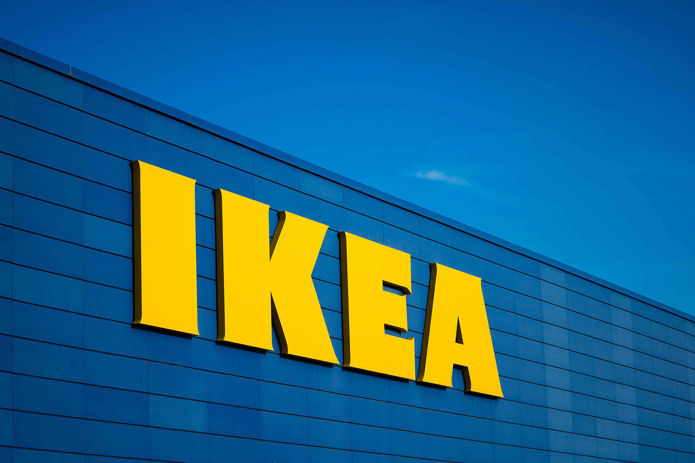 Ikea 桌布 壁紙 — 鮮黃色的IKEA標誌在晴朗藍天下，於時尚的藍色瓷磚建築上格外突出。