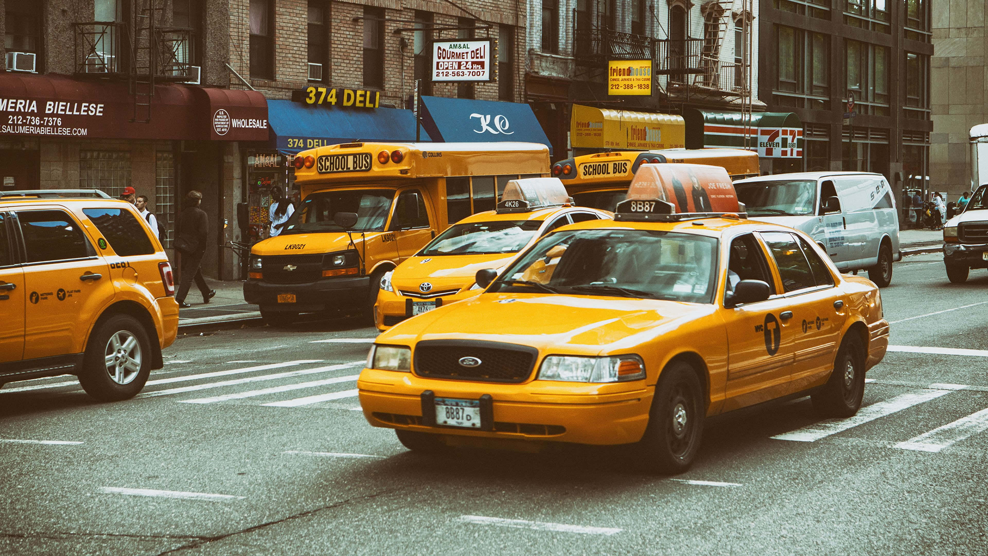 Yellow Cab 桌布 壁紙 — 鮮黃色的士和校車在繁華的城市街道上行駛，街道兩旁是磚砌建築和商店。
