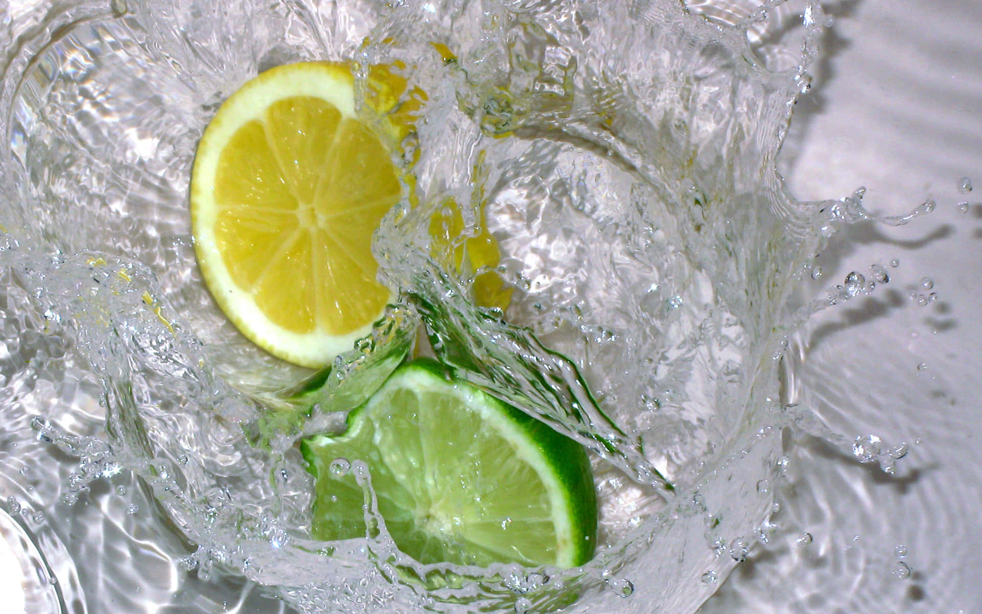 Refreshing 桌布 壁紙 — 鮮黃色的檸檬和青綠色的青檸片在清澈的水中濺起動態水花，伴隨著閃閃發光的水滴。