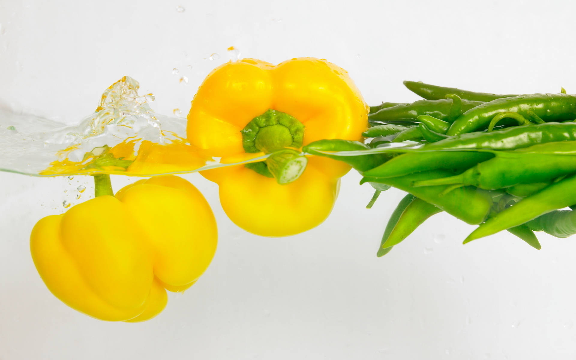 Vegetable 桌布 壁紙 — 鮮黃色的甜椒和青辣椒在清澈的水中動態飛濺，背景是純白色。