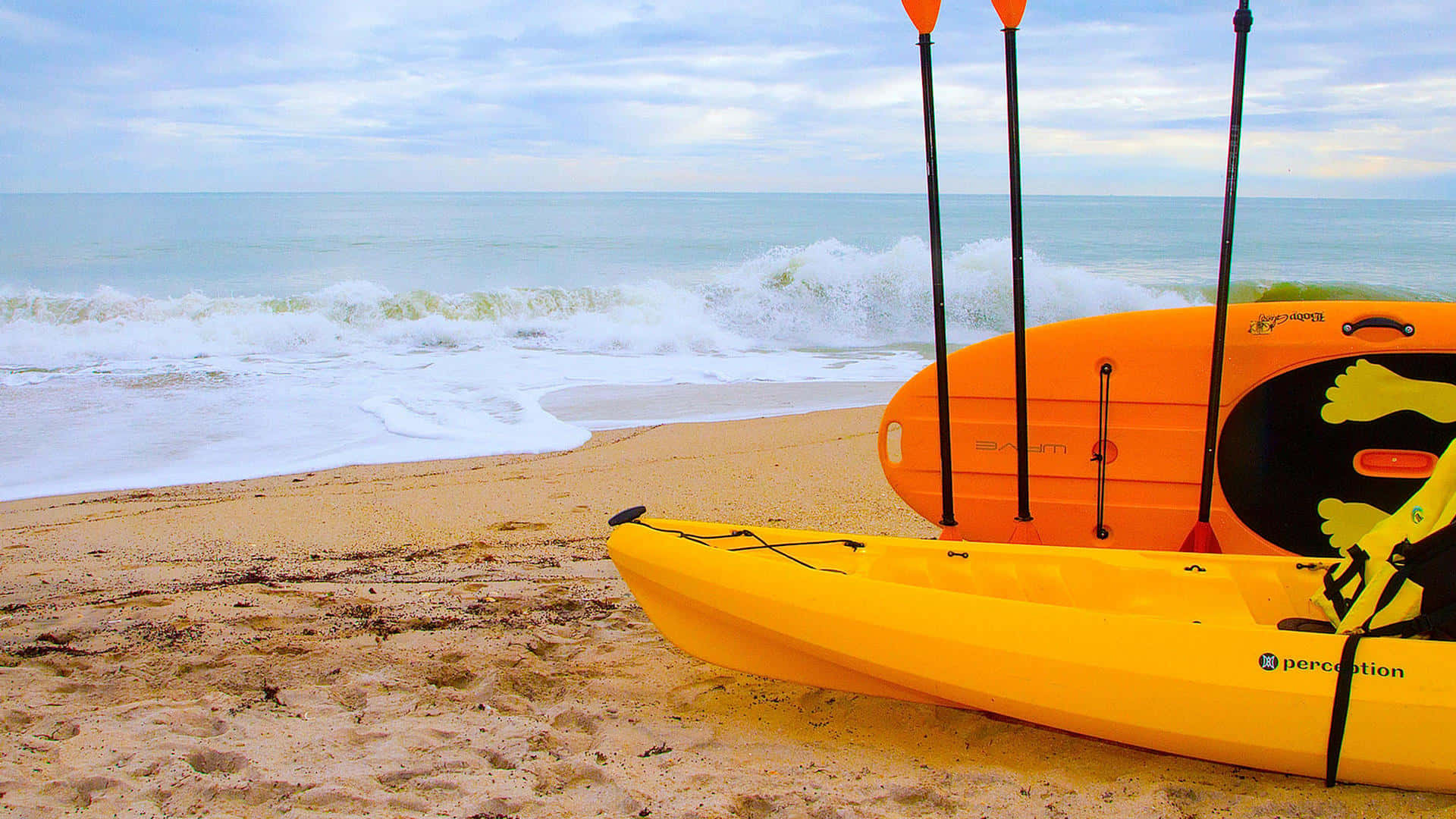 Beach Water Sports 桌布 壁紙 — 鮮黃色的皮划艇擱在沙灘上，海浪在陰天下拍打著。