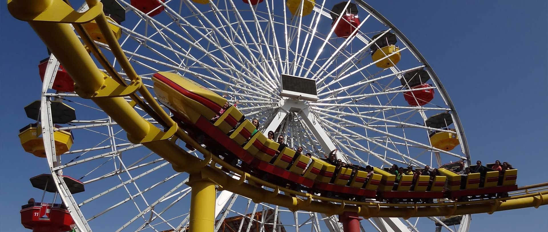 Roller Coaster 桌布 壁紙 — 鮮黃色的過山車在巨大的白色摩天輪下蜿蜒而行，背景是清澈的藍天。