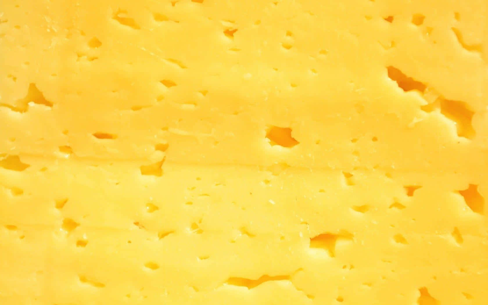 Cheese 桌布 壁紙 — 鮮黃色芝士的近距離特寫，帶有不規則孔洞和光滑質地。