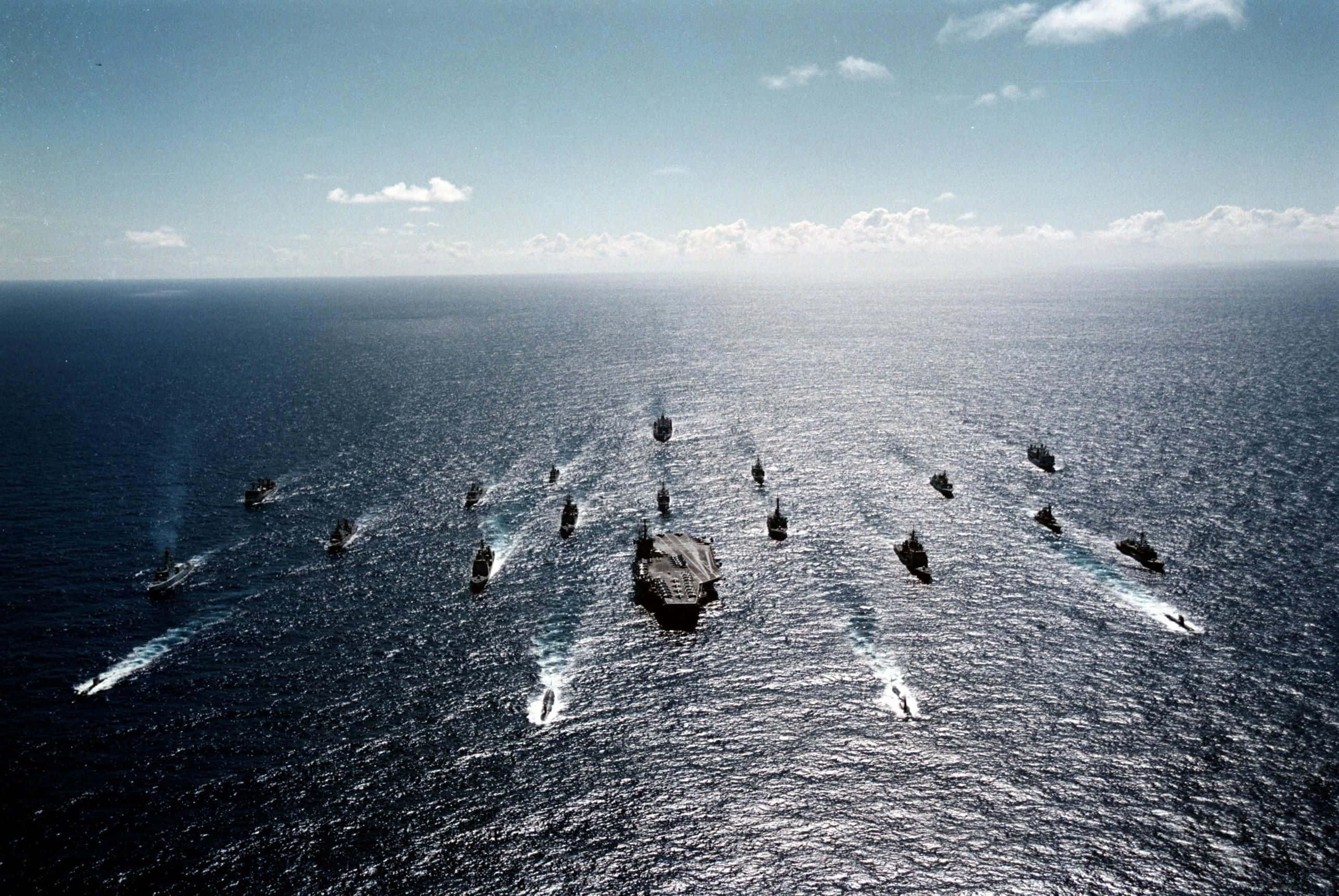 Navy 桌布 壁紙 — 鳥瞰一支以航空母艦為中心嘅海軍艦隊，喺晴朗天空下嘅廣闊藍色海洋上編隊航行。