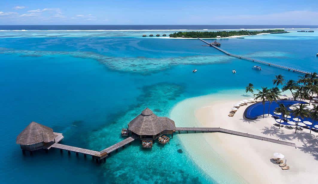 Maldives Island 桌布 壁紙 — 鳥瞰圖：豪華熱帶度假村，設有水上平房、碧綠潟湖和白色沙灘，天空清澈湛藍。