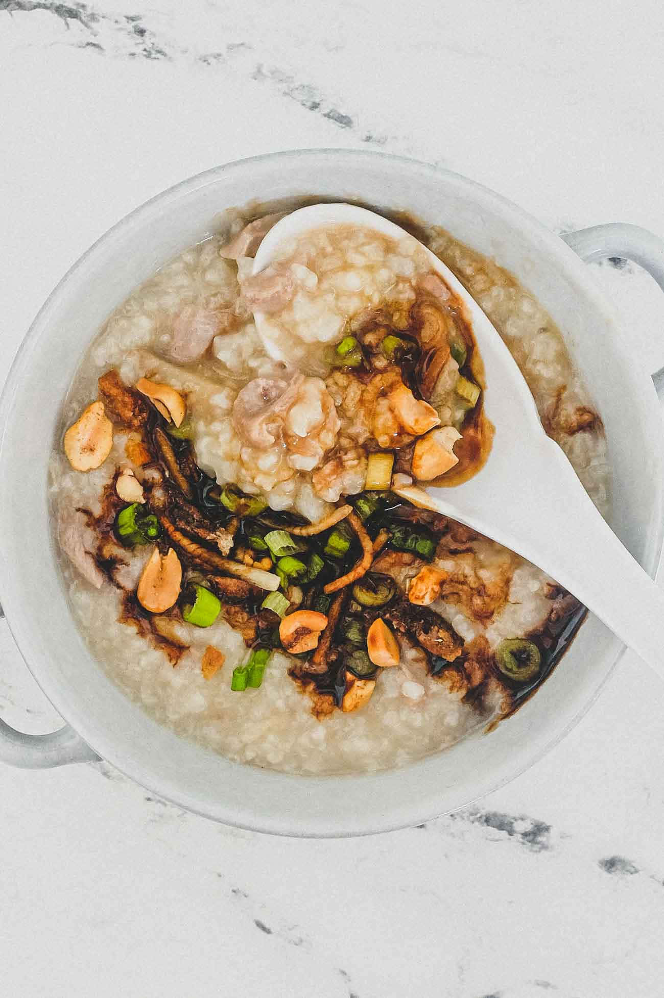 鴨肉粥俯拍視角，大理石桌面 壁紙 — 一個白色陶瓷碗盛載著 creamy 的粥，上面有花生、青蔥和深色醬汁，湯匙舀起一勺。