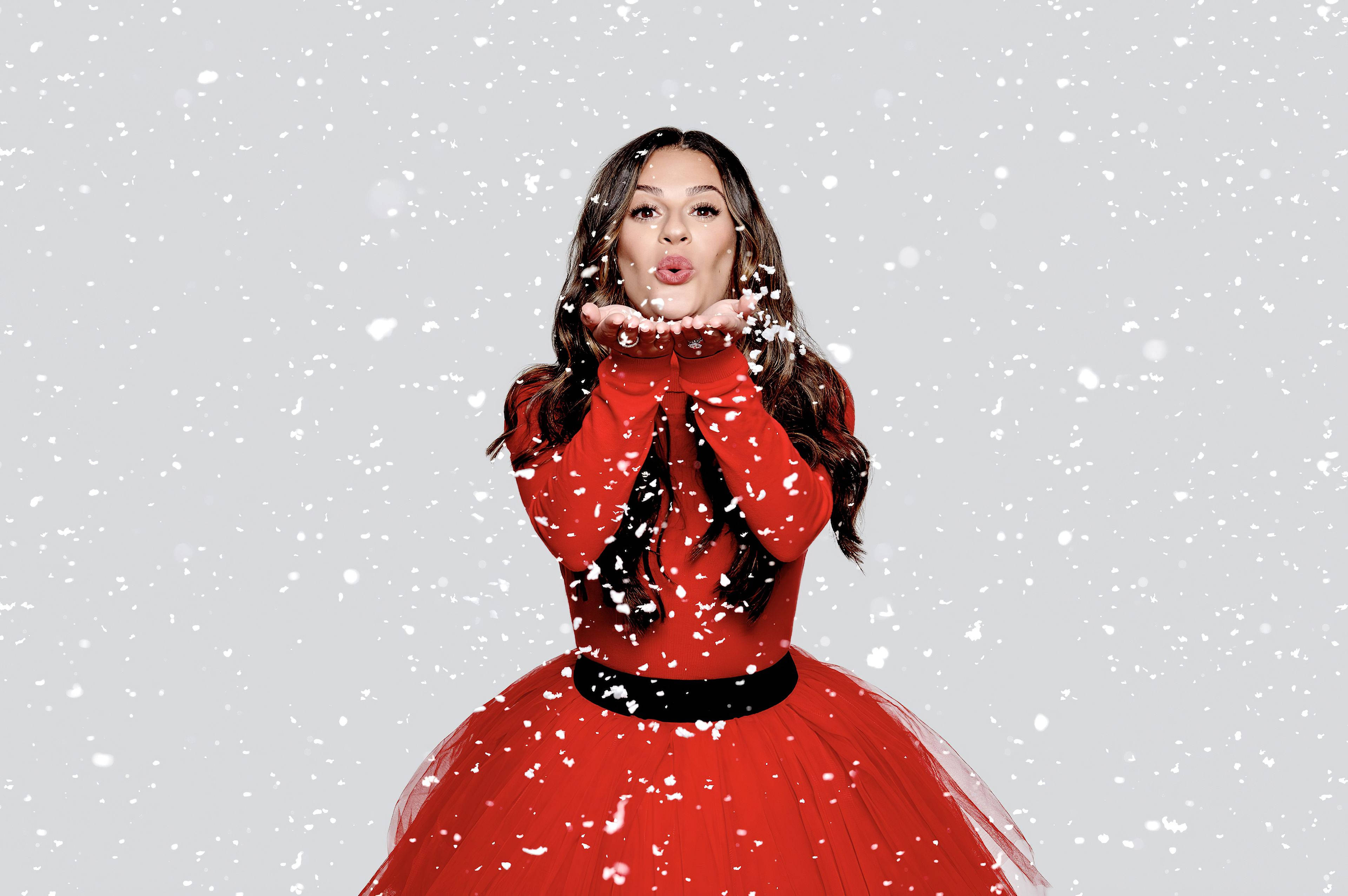 麗亞·米雪兒聖誕紅裙 壁紙 — 一位身穿鮮紅色連衣裙的女性，在白雪皚皚的灰色背景下，從她捧起的雙手中吹出雪花。