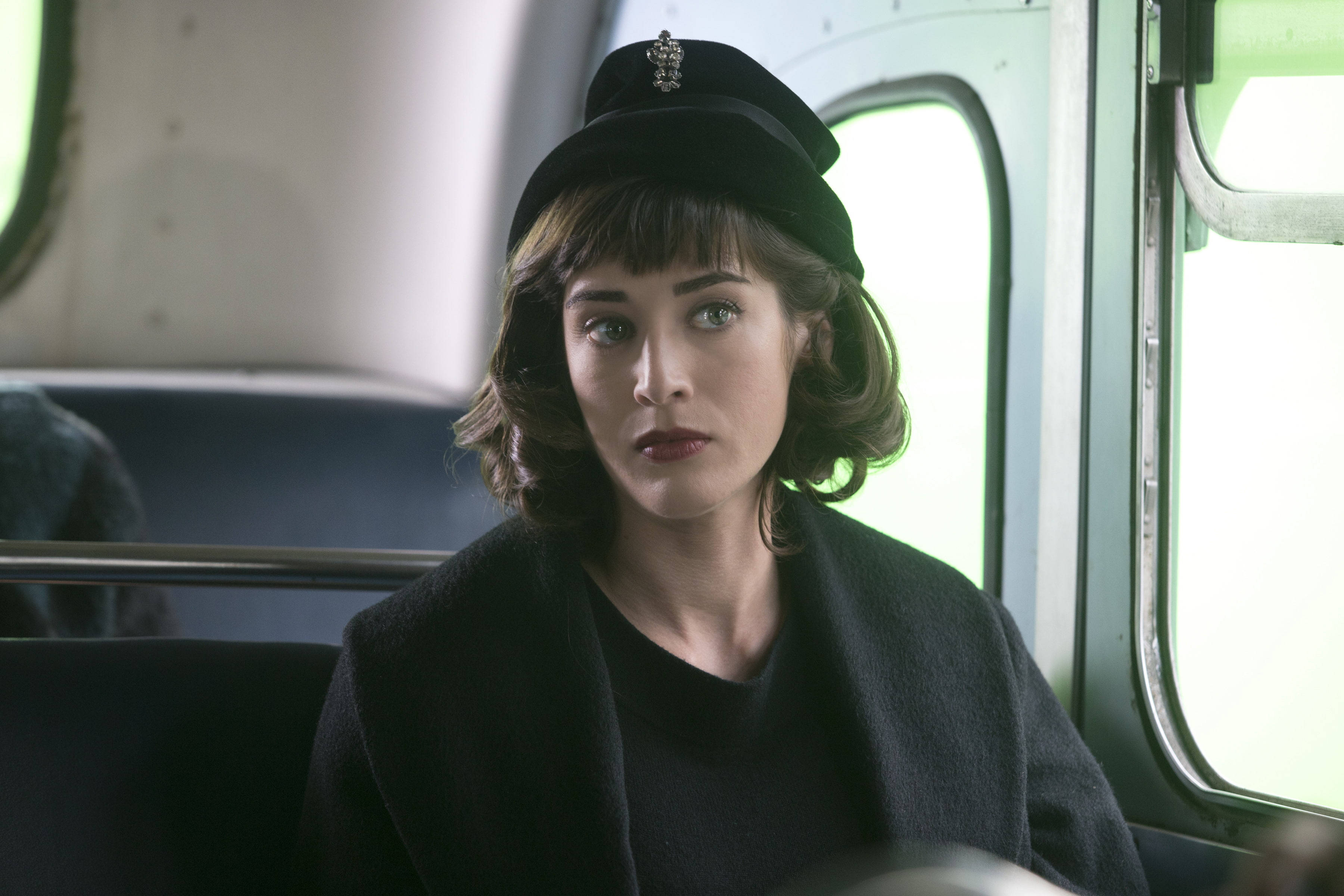 麗茲·卡普蘭出演《從海底出击》 壁紙 — 一位戴黑色帽子和穿黑色外套的女性在綠色邊框窗戶的復古火車車廂內若有所思地凝視。