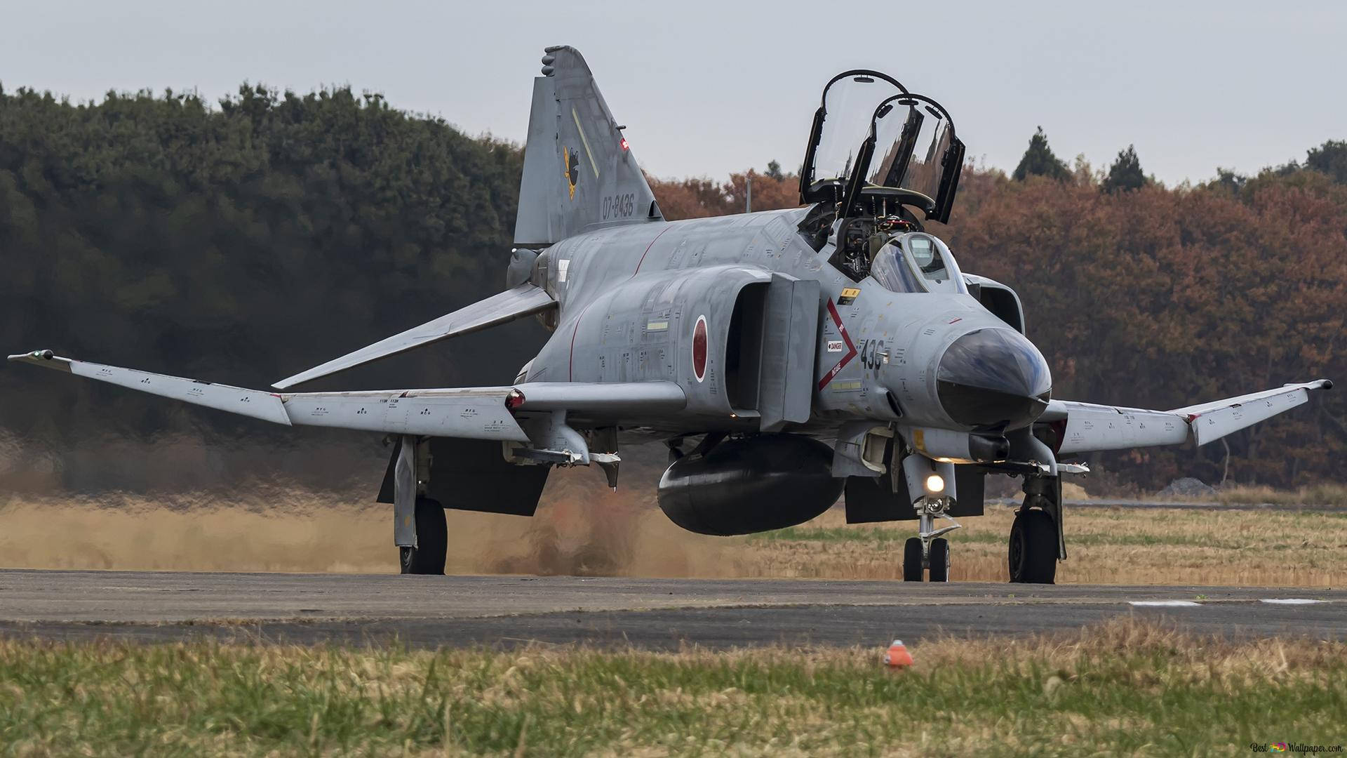 麥克唐納道格拉斯F-4幽靈II戰鬥機 1920x1080 壁紙 — 一架灰色日本戰鬥機在跑道上滑行，揚起灰塵，背景是秋天的樹木。