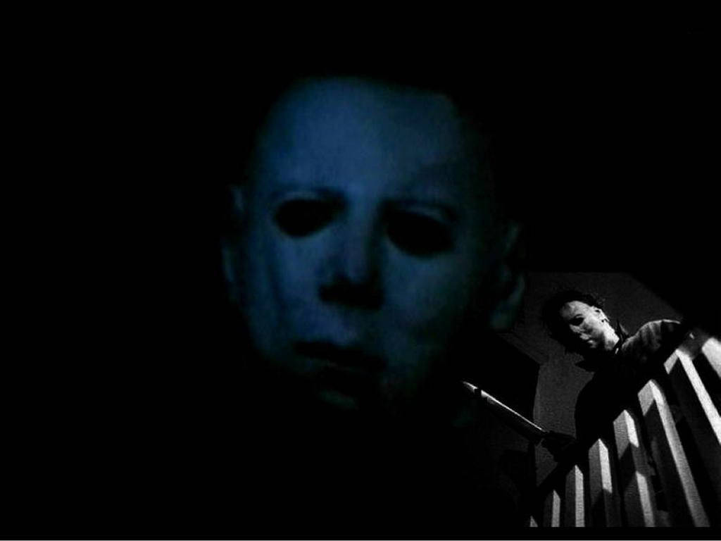 Michael Myers 在黑暗的藍色恐怖場景中，戴著面具，籬笆後面還有另一個人影。