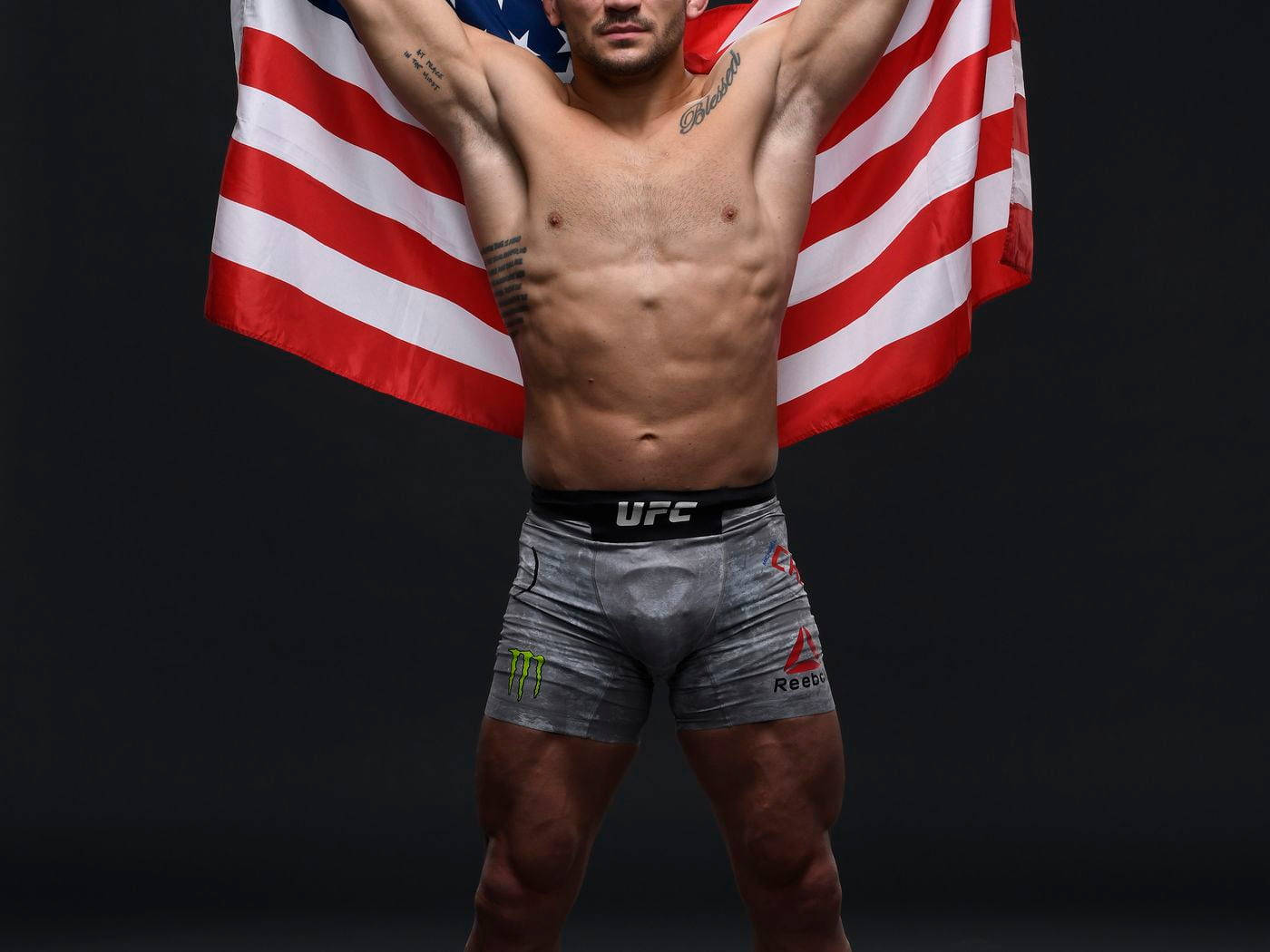 運動型男性拳手在黑暗背景下穿著UFC短褲手持美國國旗。