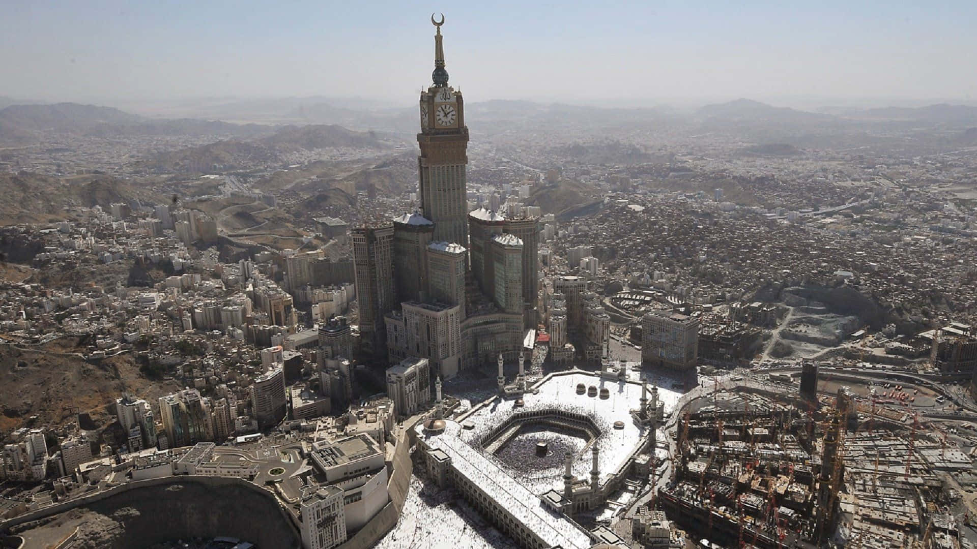 Makkah 桌布 壁紙 — 麥加阿布拉吉阿爾貝塔樓和卡巴天房的鳥瞰圖，朝聖者在晴朗的天空下繞行聖地。