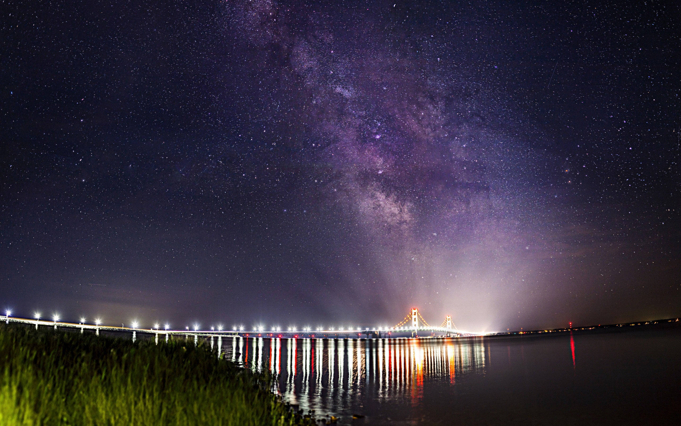 麥基那橋星夜美景 壁紙 — 銀河在星空下平靜的水面上拱起一座發光的橋樑，倒映在水中。