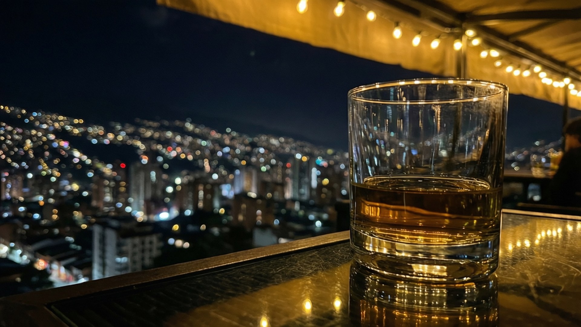 屋頂酒吧上的威士忌杯，背後是模糊的城市夜景。