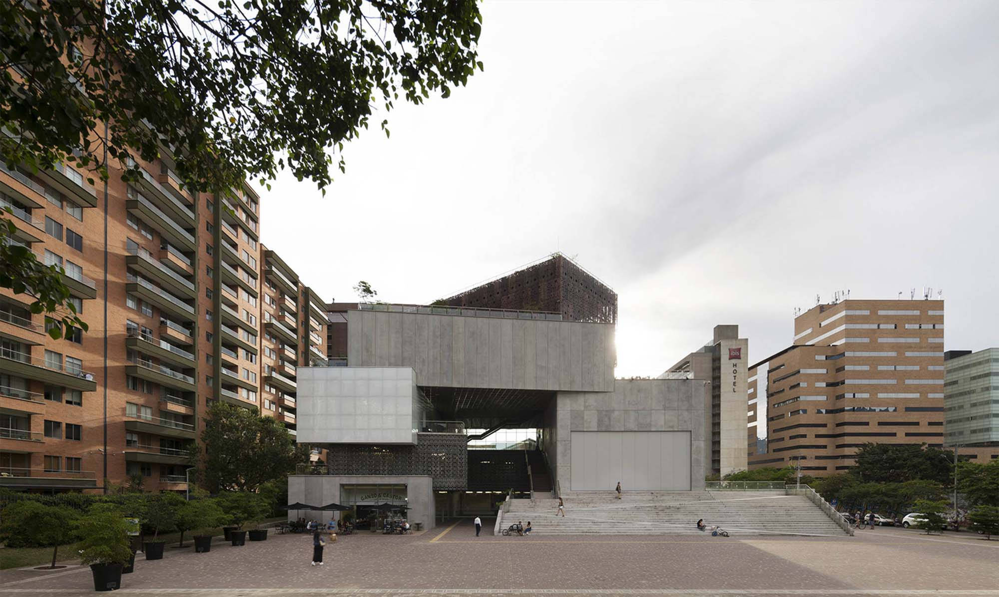 麥德林現代藝術博物館 壁紙 — 現代混凝土和玻璃建築結構，幾何形狀，矗立在城市廣場，周圍是住宅建築和綠化，天空多雲。