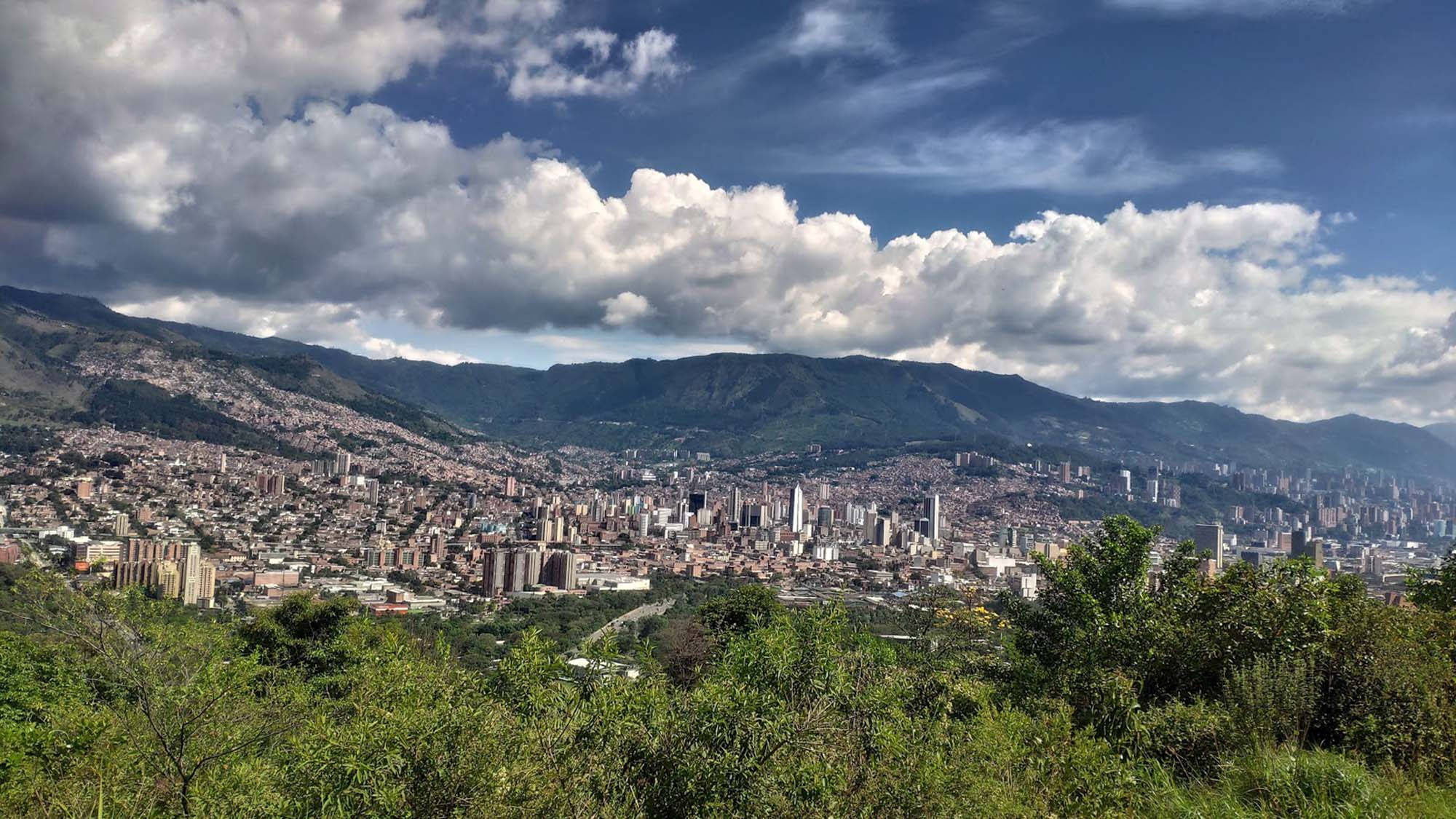 麥德林艾爾沃拉多山景觀 壁紙 — 一座廣闊的城市依附在山坡上，天空戲劇性，充滿蓬鬆的白雲。