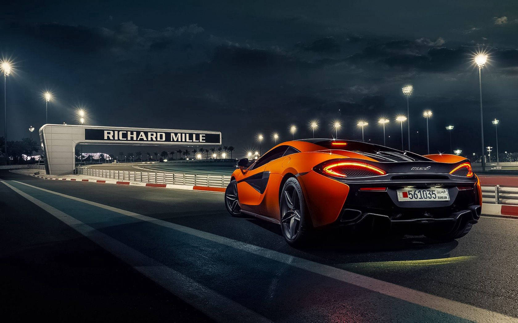 夜間在Richard Mille標誌下，橙色McLaren賽車在燈光璀璨的賽道上。