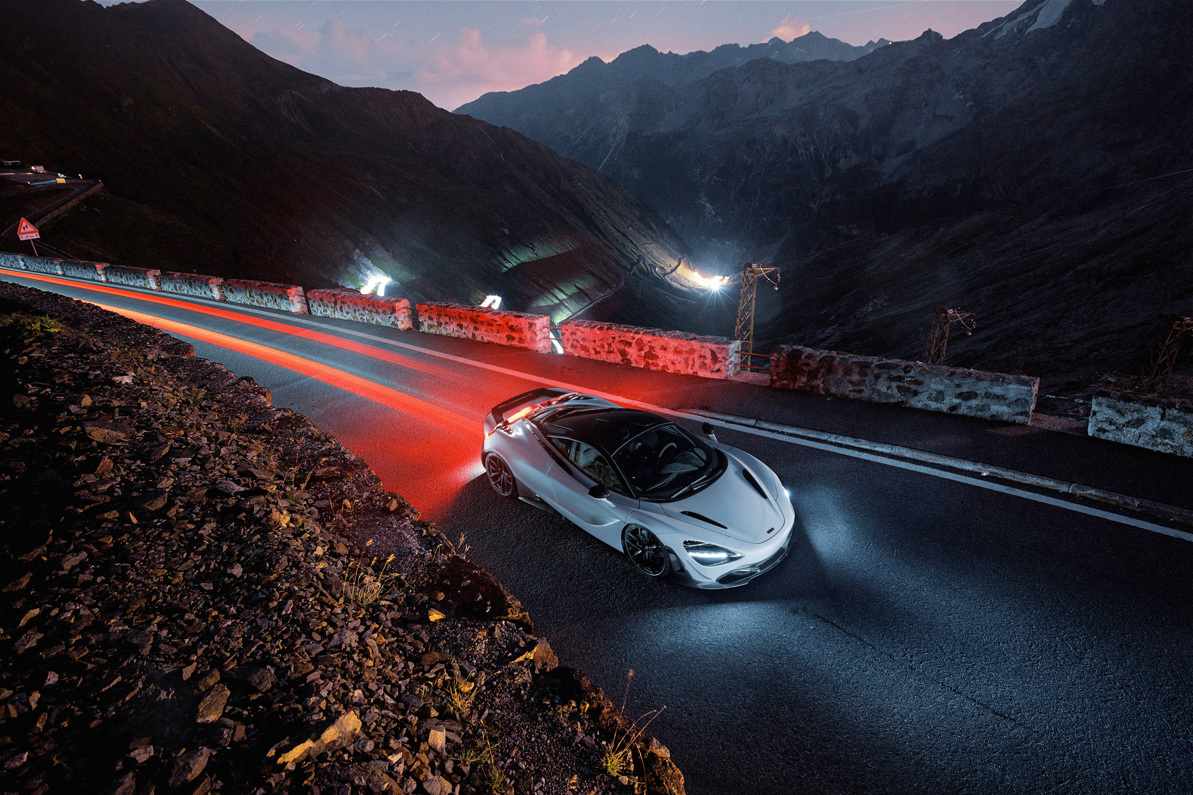 麥拉倫720S 白夜風景 壁紙 — 一輛銀色跑車在黃昏時沿著山路滑行，身後留下紅色光跡。