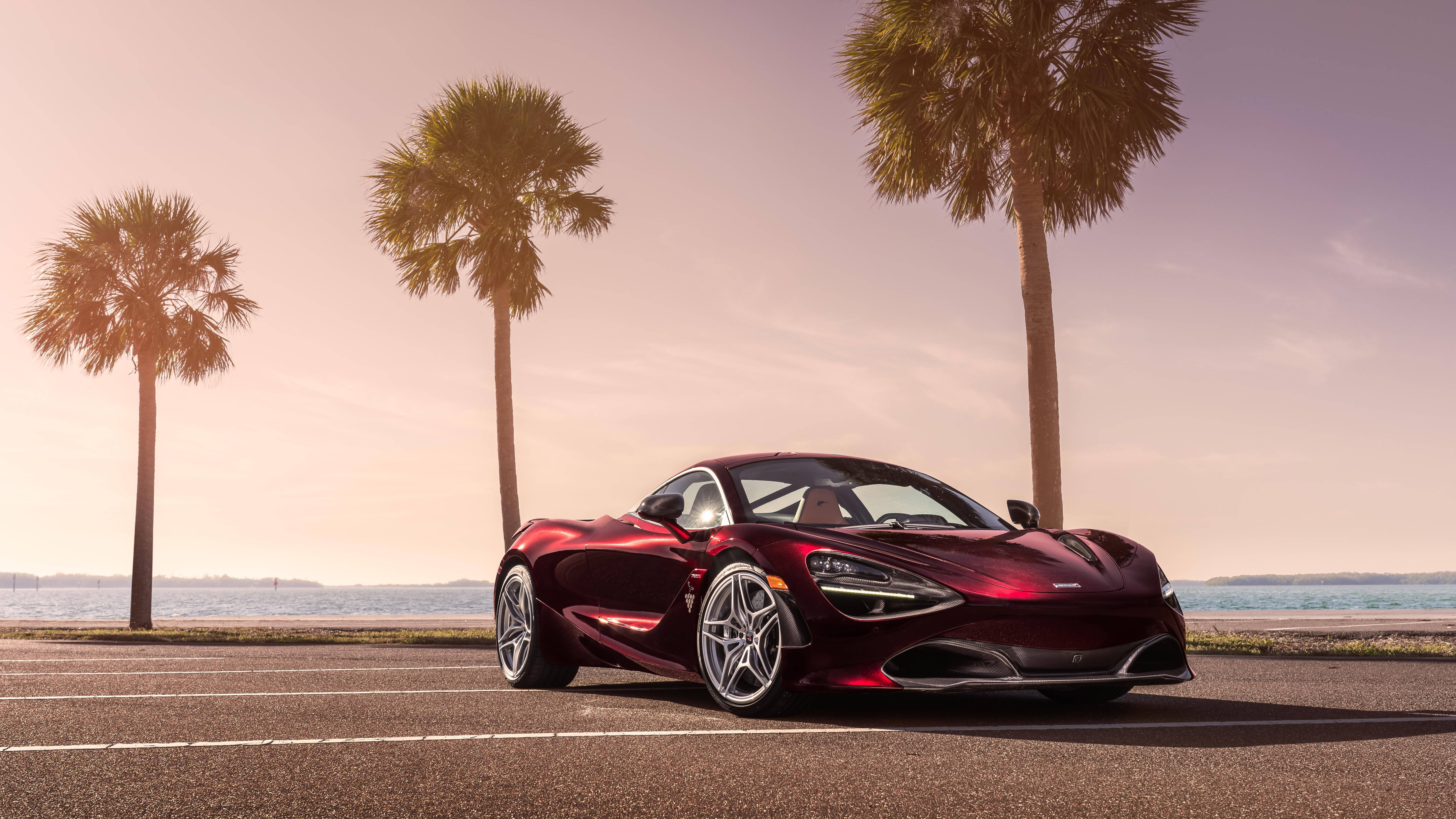 麥拉倫720S 紫紅色 壁紙 — 一架亮紅色McLaren 720S跑車停泊在日落時分的海岸道路上，背景有棕櫚樹和海洋。