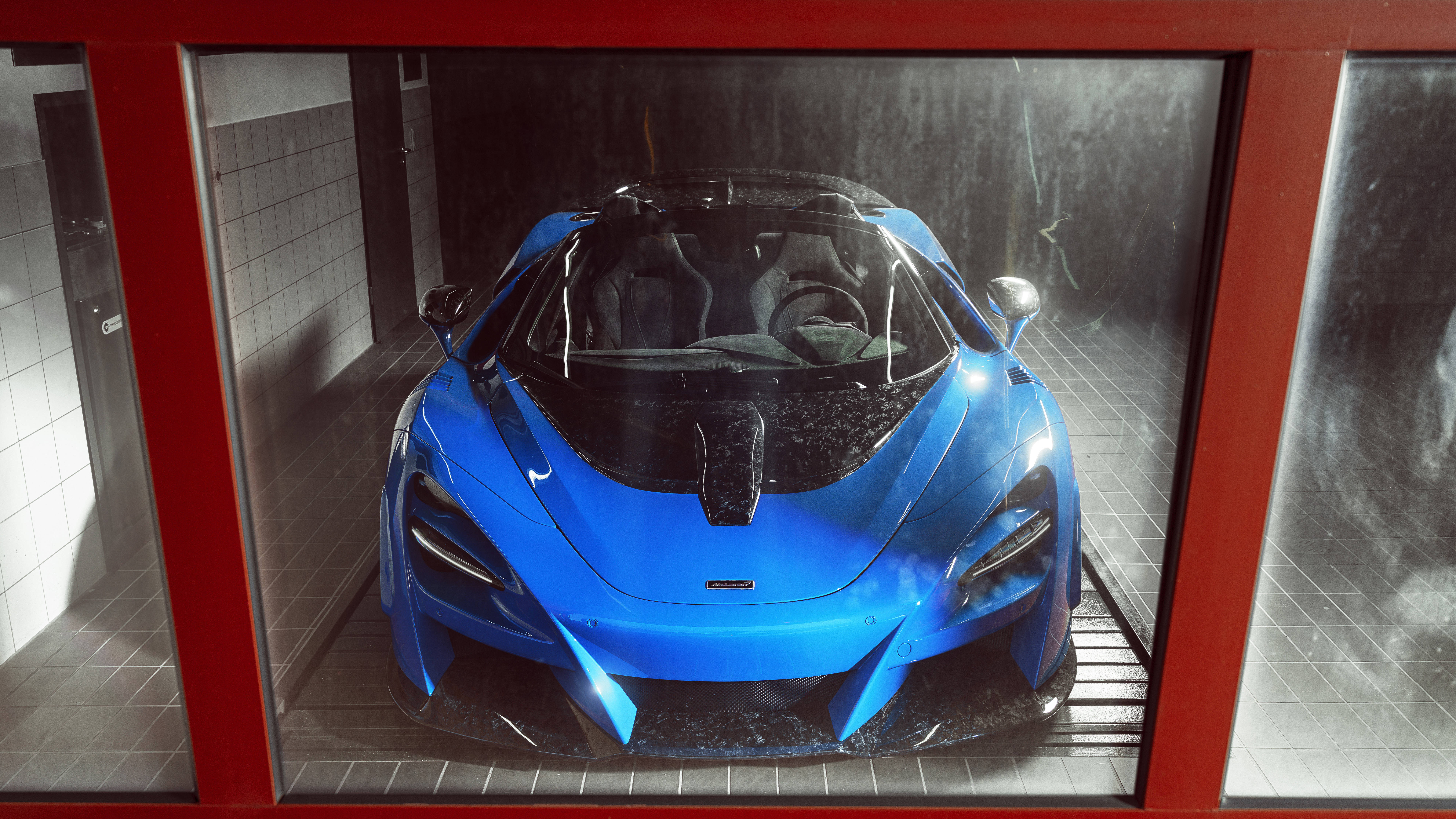 麥拉倫720S 藍色展廳 壁紙 — 一輛充滿活力的藍色McLaren跑車在紅色框架玻璃展示櫃內，於攝影棚燈光下閃閃發光。