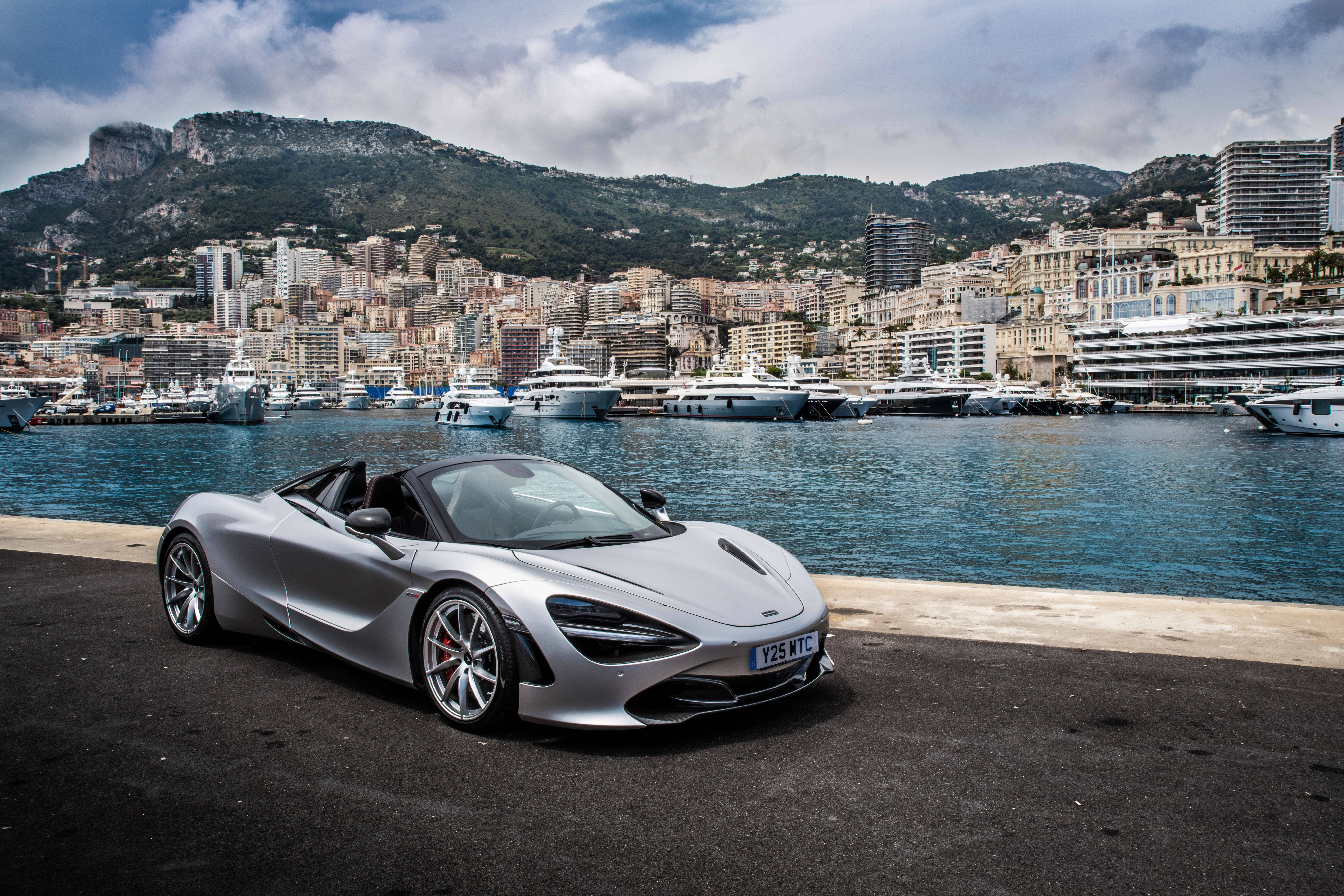麥拉倫720S 銀色碼頭 壁紙 — 一架時尚的銀色McLaren 720S Spider停在海濱長廊上，背景是豪華遊艇和密集的沿海城市景觀。