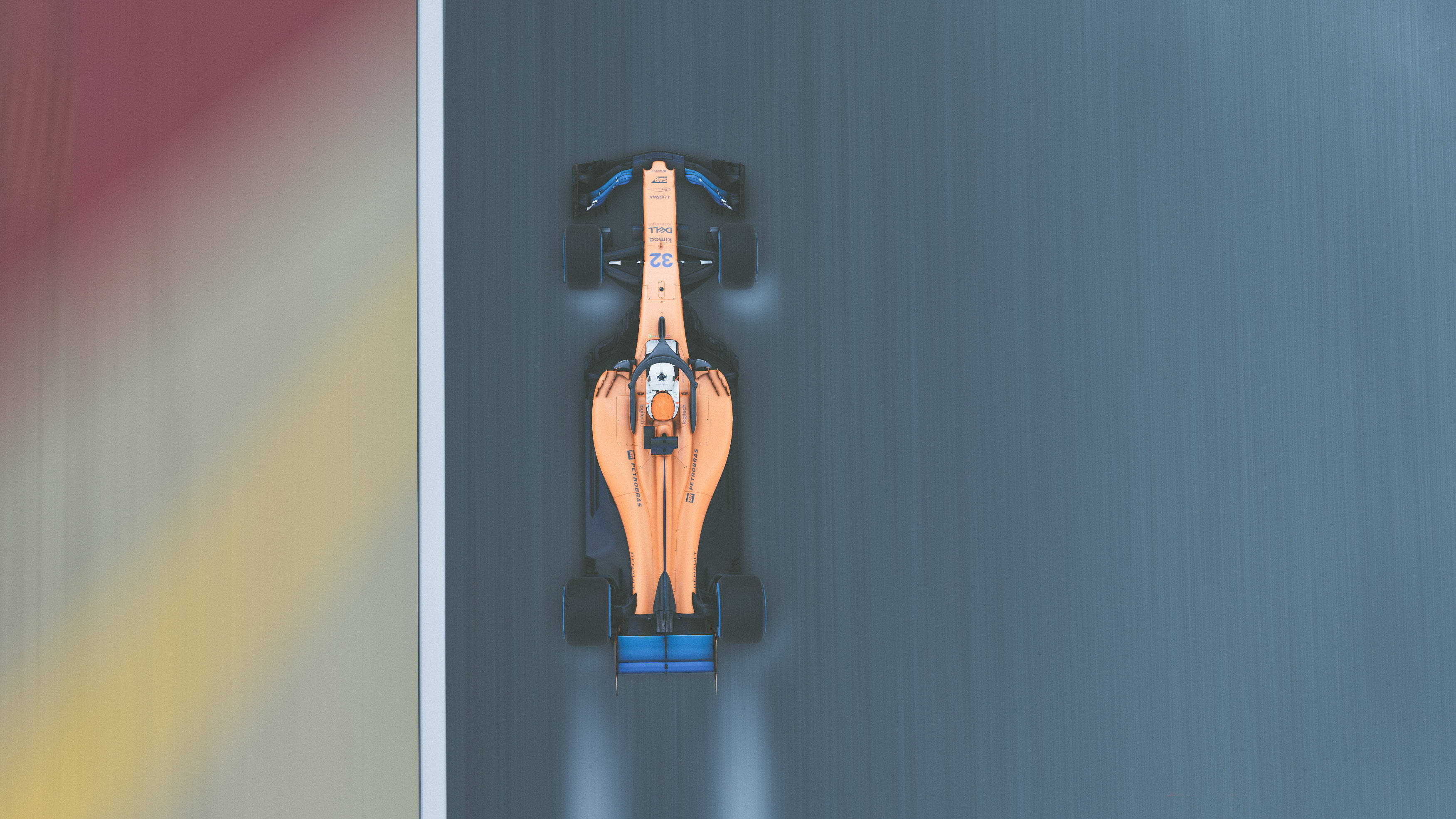 麥拉倫F1賽車空中拍攝 壁紙 — 從上方俯瞰一輛橙色和藍色的F1賽車在賽道上疾馳，帶有動態模糊效果。