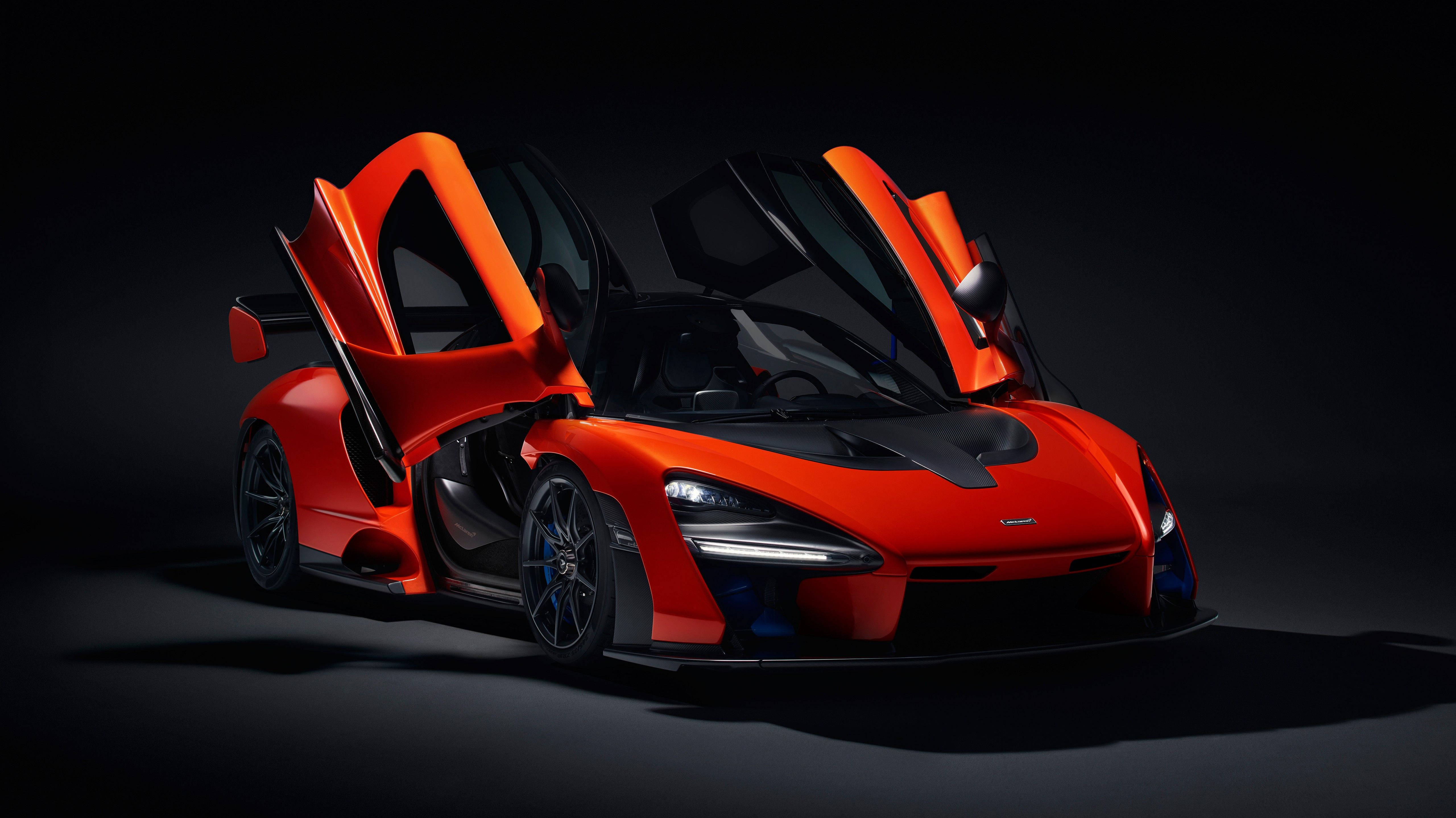 麥拉倫橙色塞納 壁紙 — 一輛引人注目的橙色McLaren Senna超級跑車，鷗翼門打開，在黑色背景下被戲劇性的工作室燈光照亮。