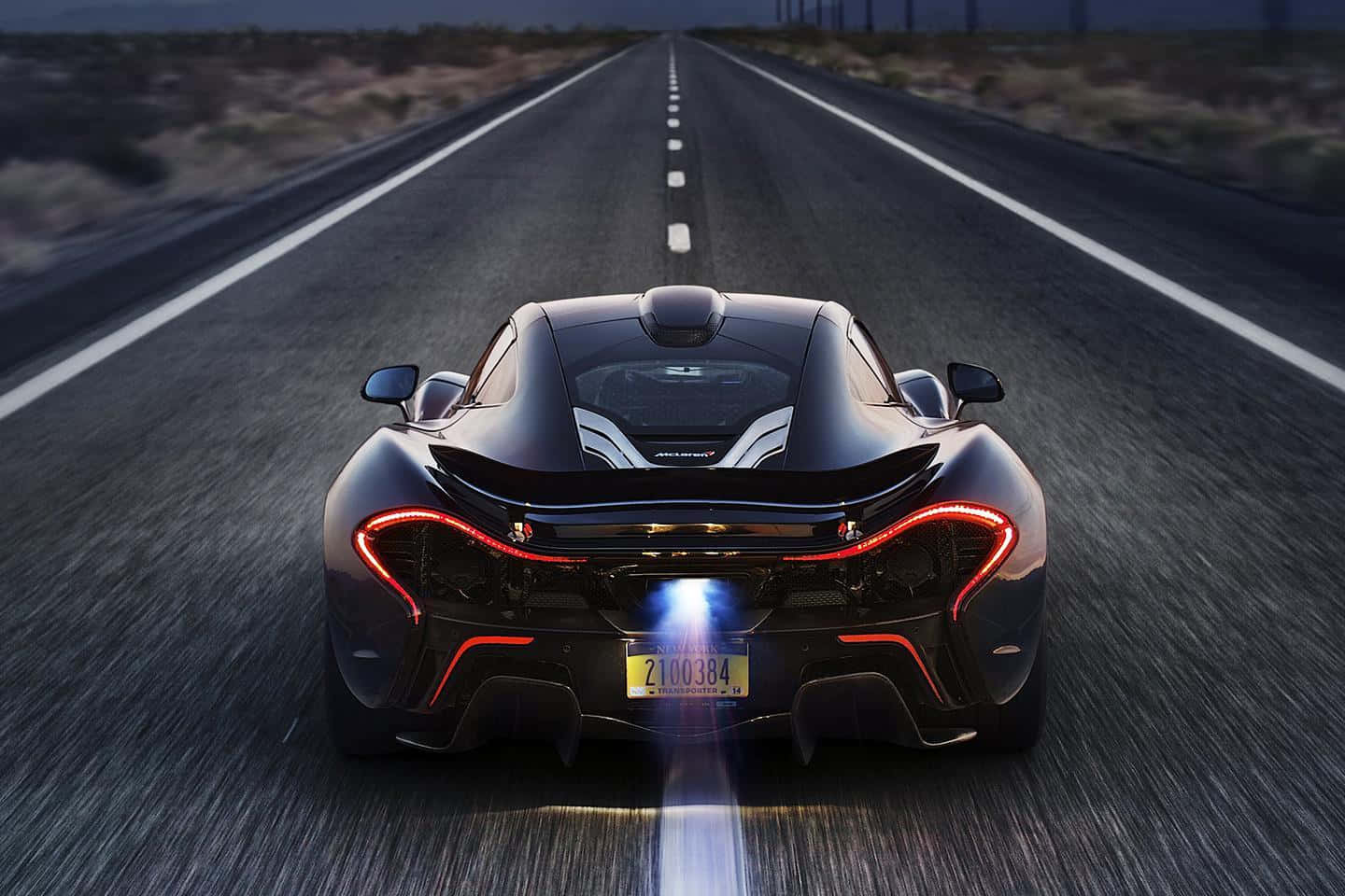 黑色McLaren P1在黃昏時分沿著沙漠高速公路飛馳，帶有發光的燈光。