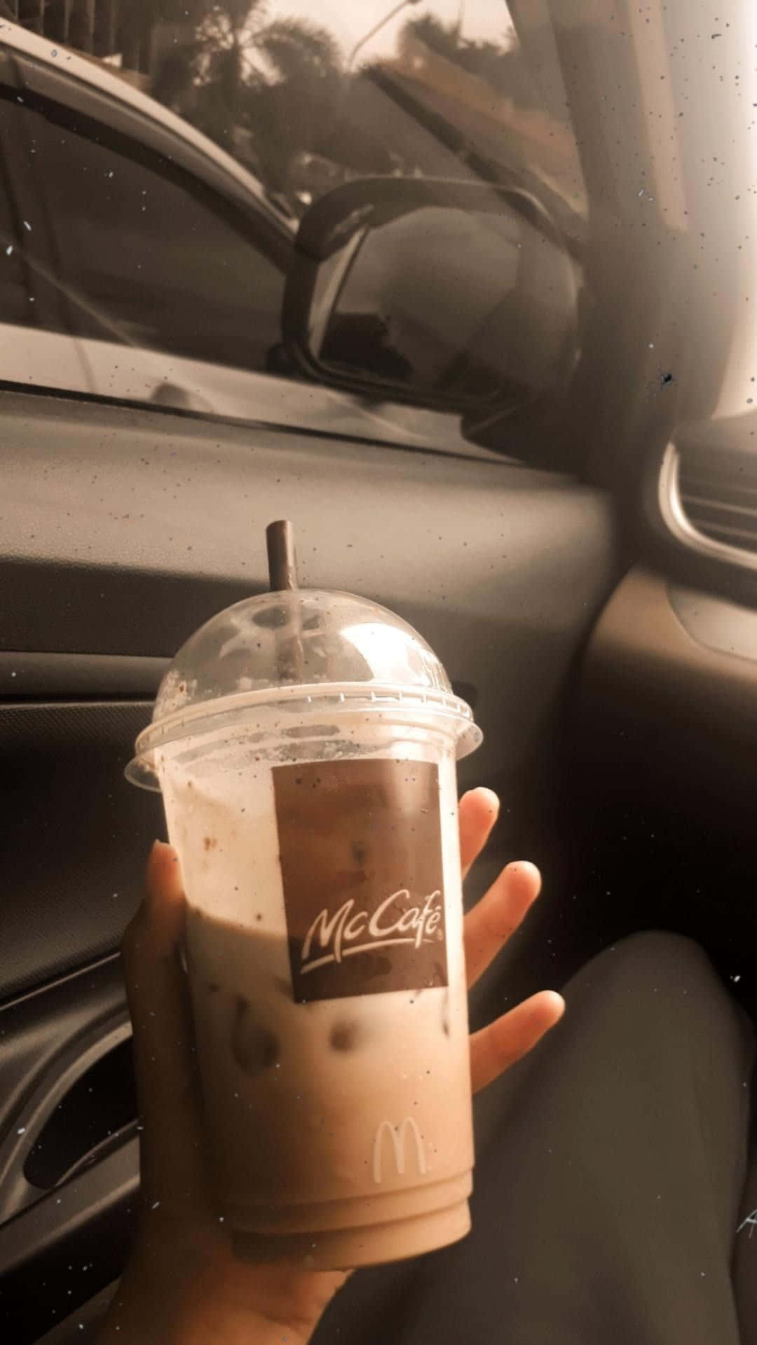 麥當勞McCafé飲品餐點圖片 壁紙 — 一隻手在車內拿著McCafé凍咖啡，溫暖的陽光透過窗戶照射進來。