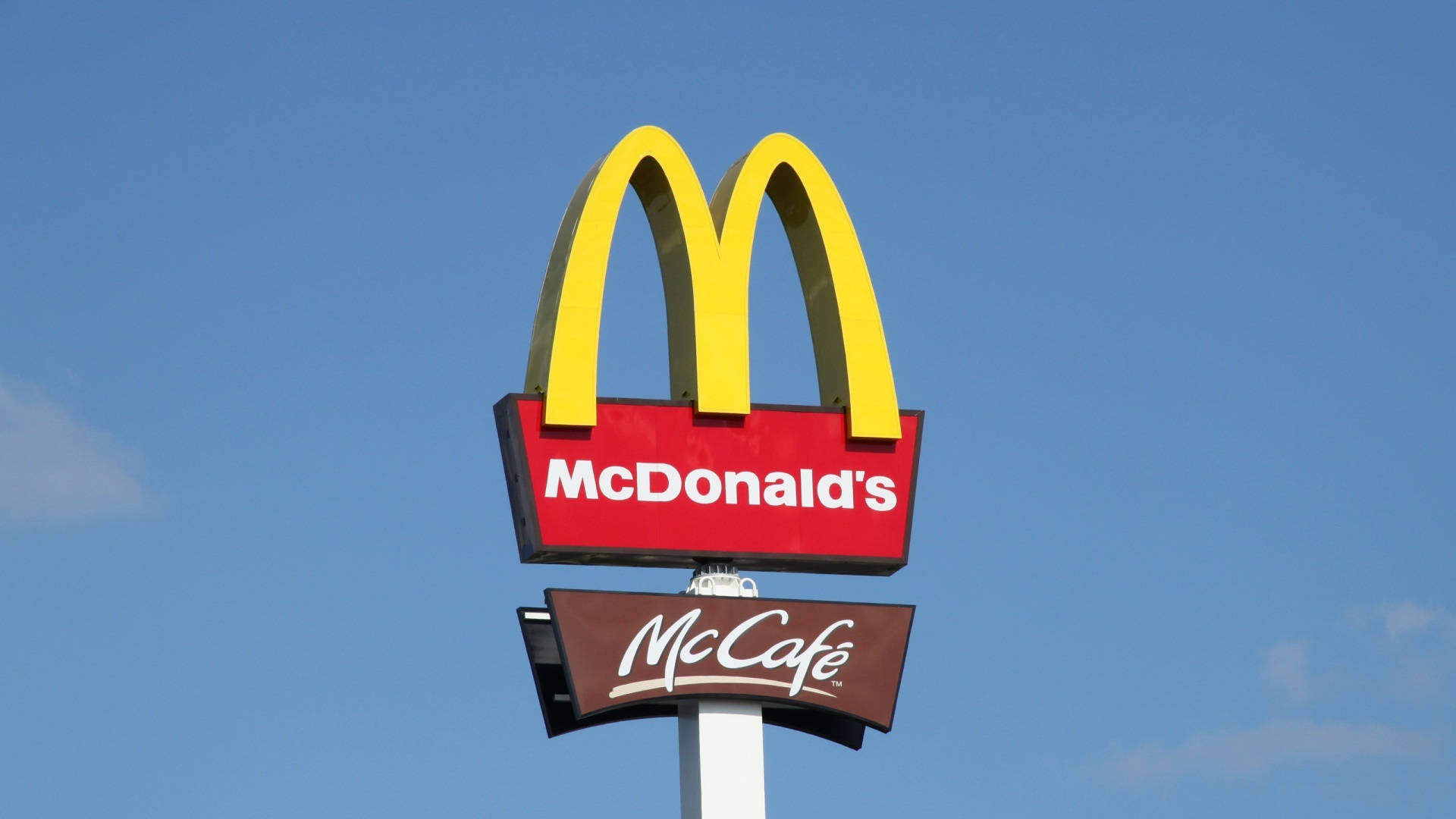 麥當勞McCafe招牌 壁紙 — 一個鮮黃色的麥當勞拱門標誌和帶有白色文字的紅色招牌，在清澈的藍天下格外醒目。