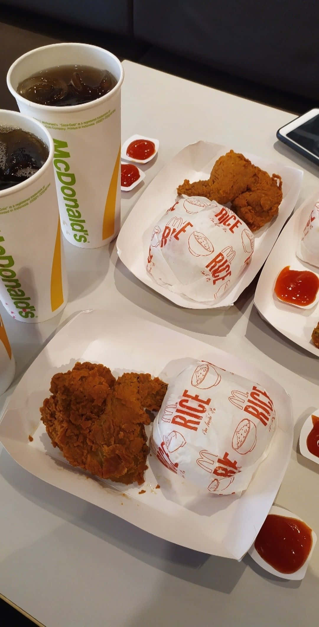 麥當勞雞肉配飯餐點 壁紙 — 麥當勞炸雞飯碗和冰凍飲品放在白色桌子上，旁邊有茄汁包的特寫。