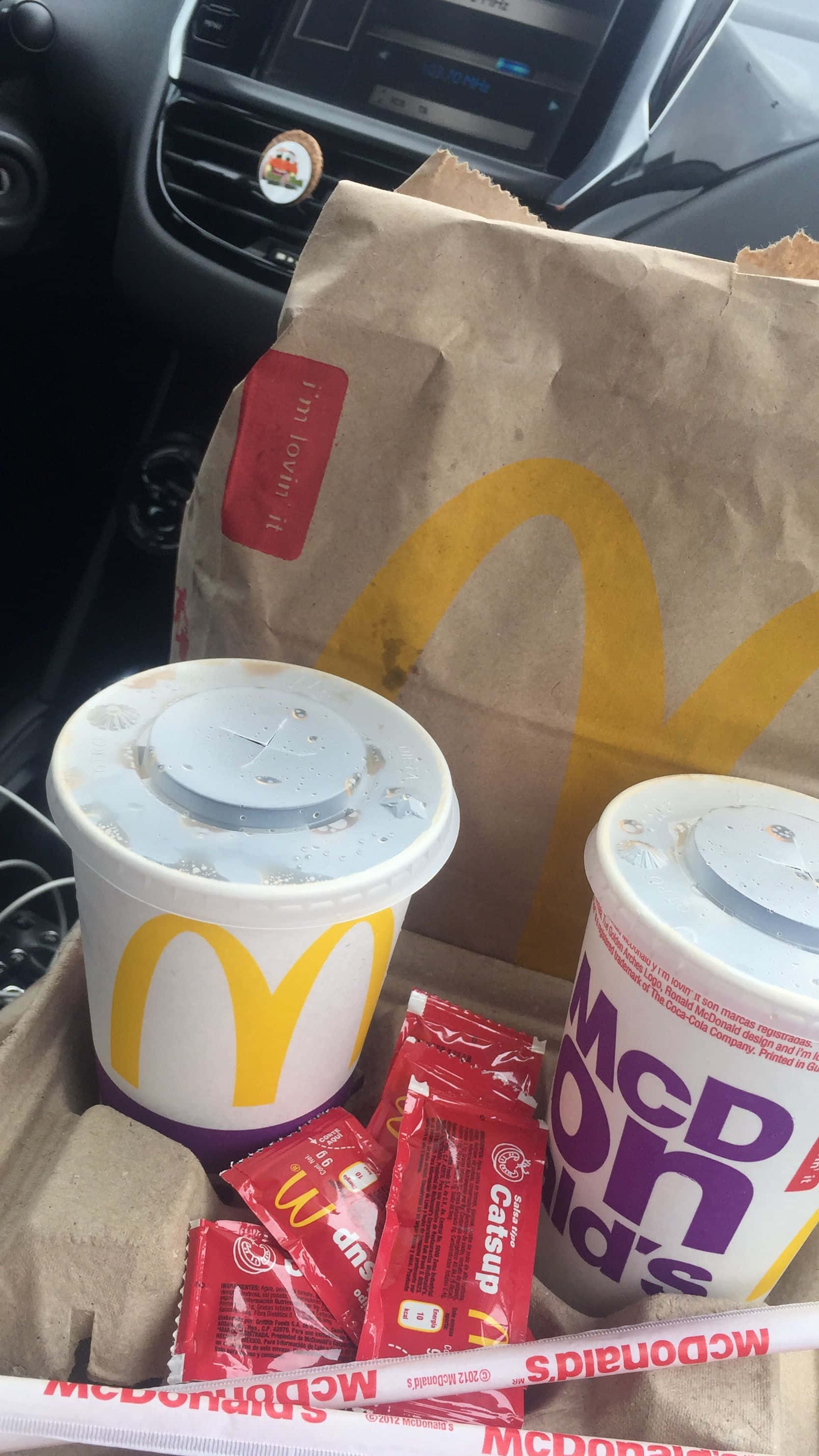 麥當勞飲品與番茄醬 壁紙 — 麥當勞薯條和飲品放在車內的紙板托盤上，儀表板清晰可見。