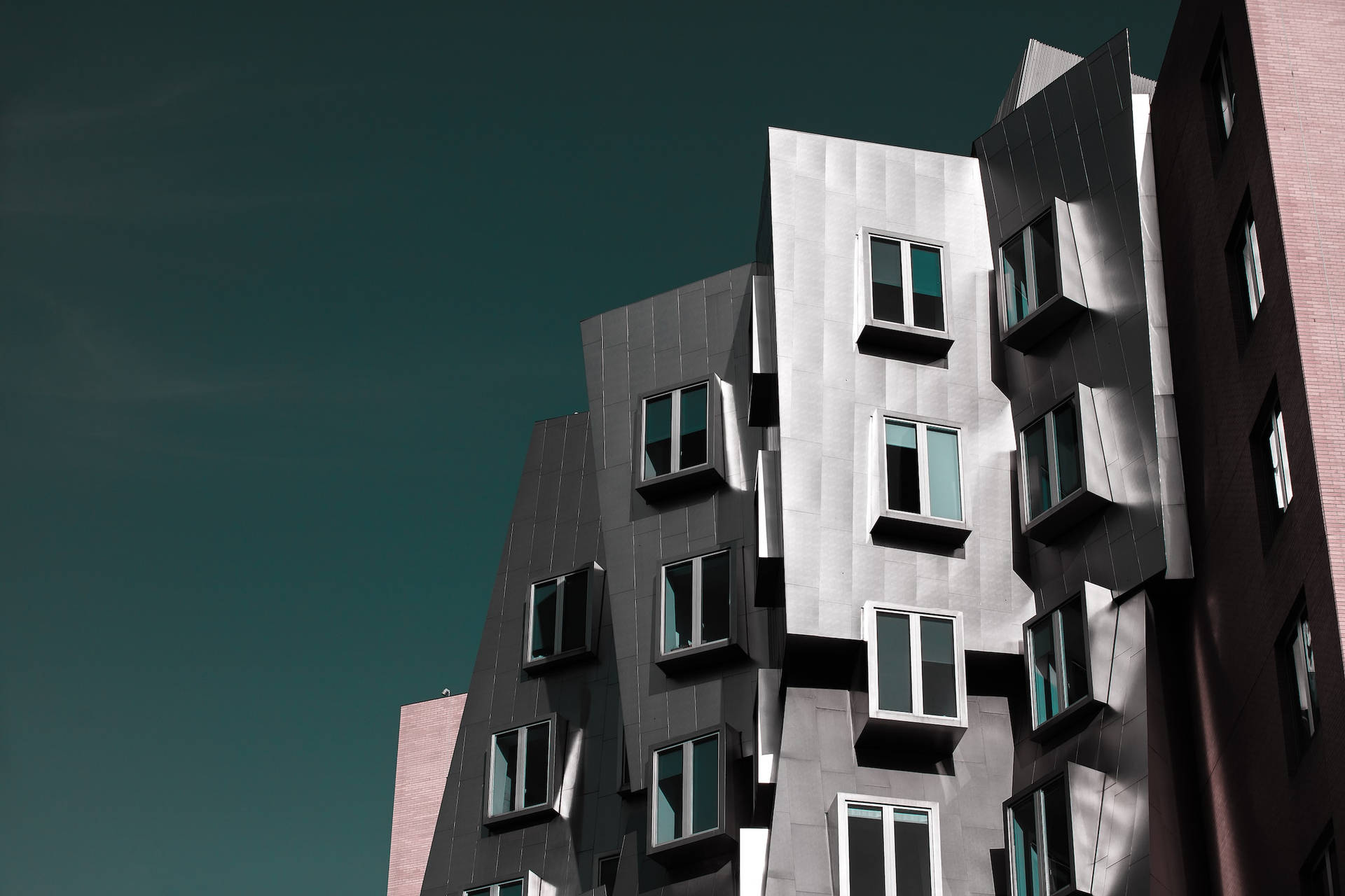 現代棱角建築，帶有金屬面板和窗戶，在藍綠色天空下。