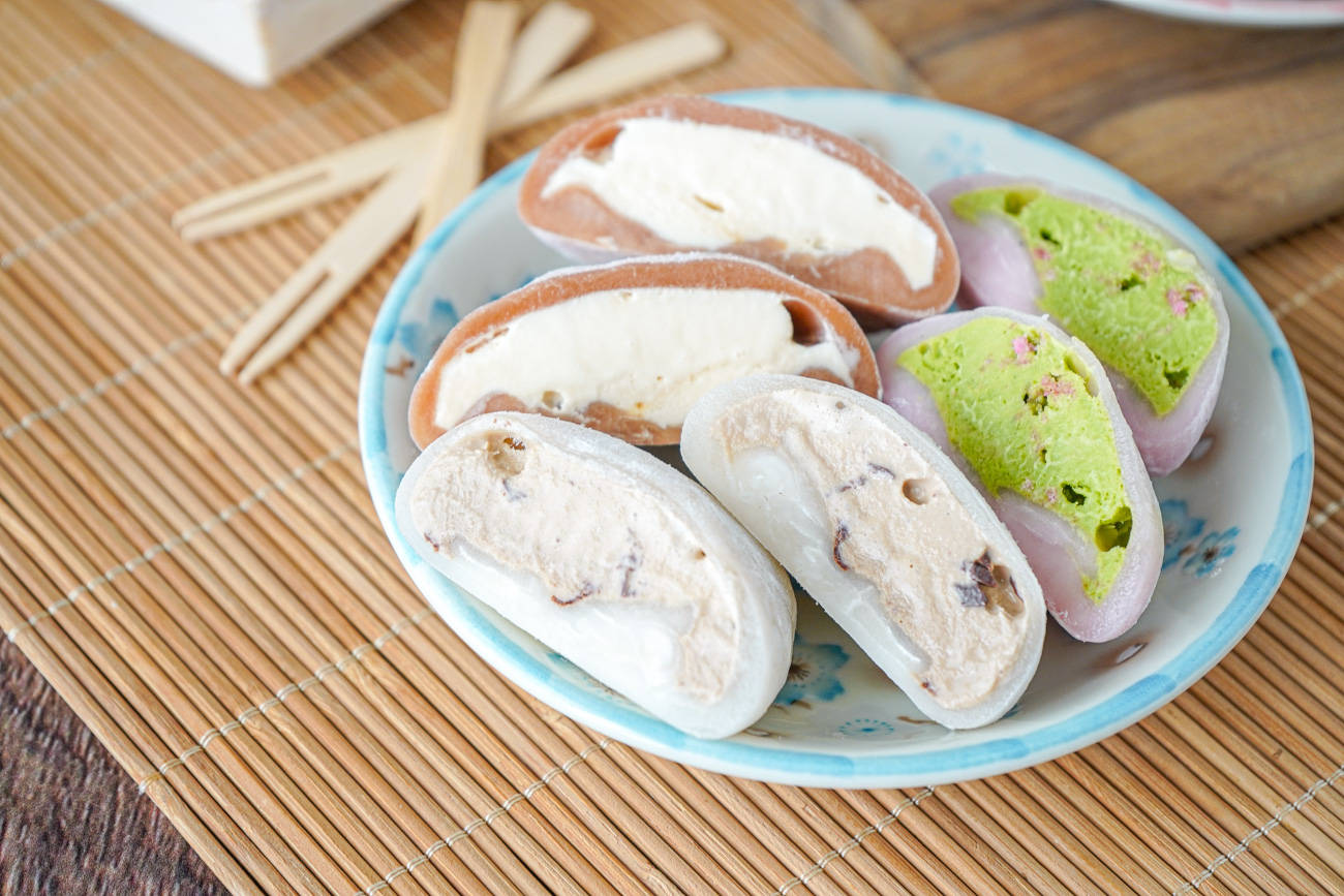 一盤各式各樣有奶油餡料的麻糬甜品放在竹蓆上。