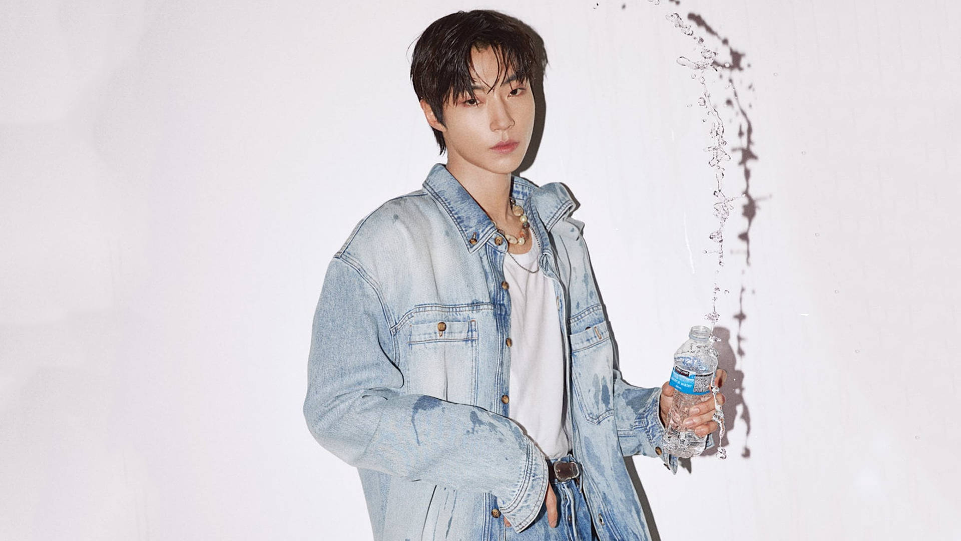 黃仁燁 W Korea 牛仔系列 壁紙 — 一位身穿牛仔外套的年輕男子手持水瓶，液體在他身後戲劇性地弧線飛濺，背景為純白色。